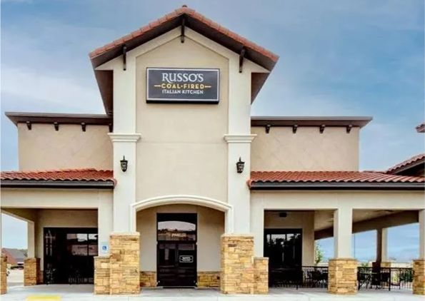 Exterior of Russo's Coal Fired Italian Kitchen restaurant; beige stucco, brown roof, signage, columns, and seating area.