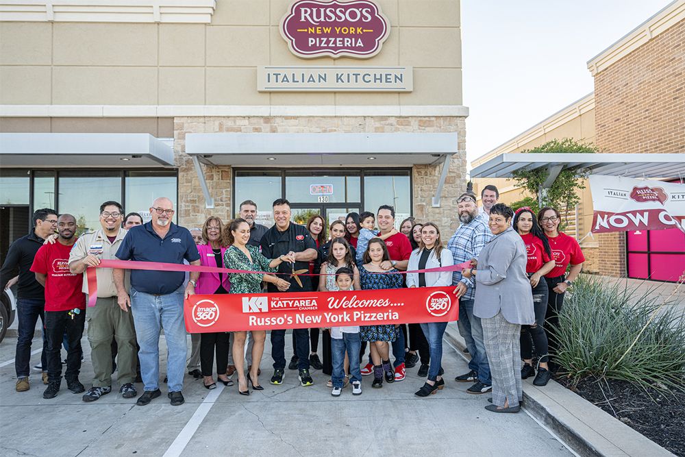 People cut a ribbon in front of a Russo's Pizzeria restaurant, celebrating its grand opening.