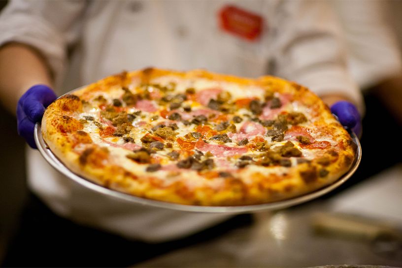 A chef holding a cooked pizza on a metal pan.