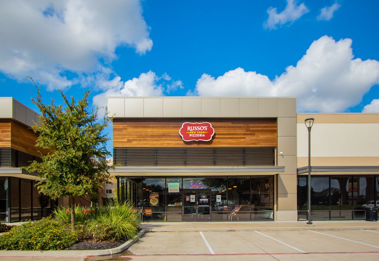 A retail store with a wooden facade and large windows, under a blue sky. The store's sign reads 