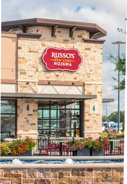 Russo's New York Pizzeria building exterior with brick facade, red sign, and window seating area.