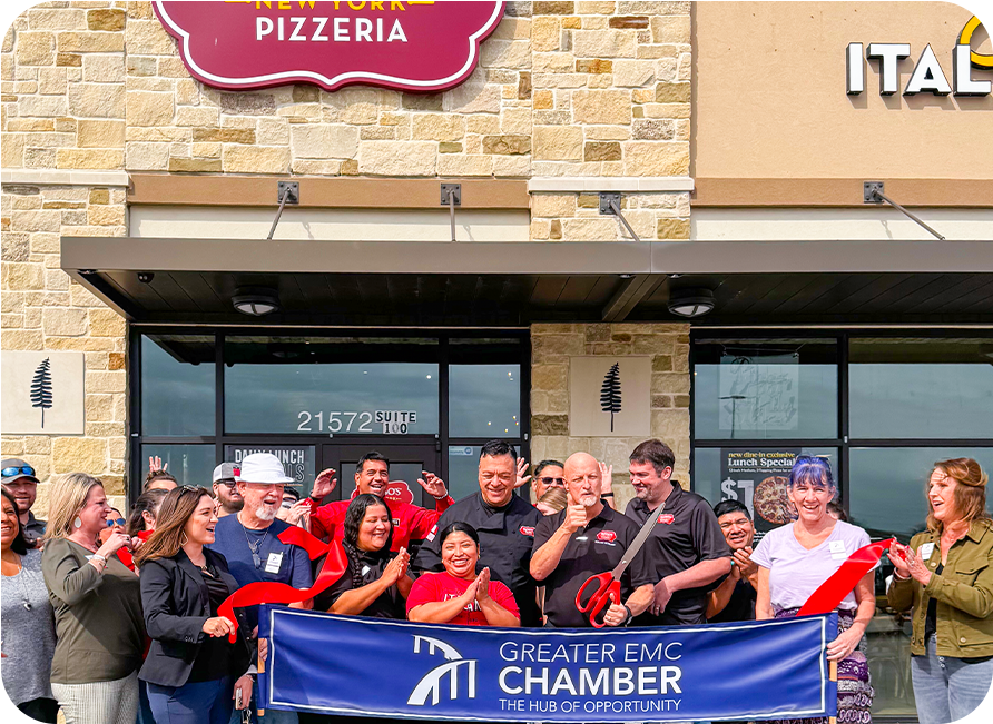 Ribbon-cutting ceremony at New York Pizzeria, exterior shot. People clap; building features a stone facade and awning.