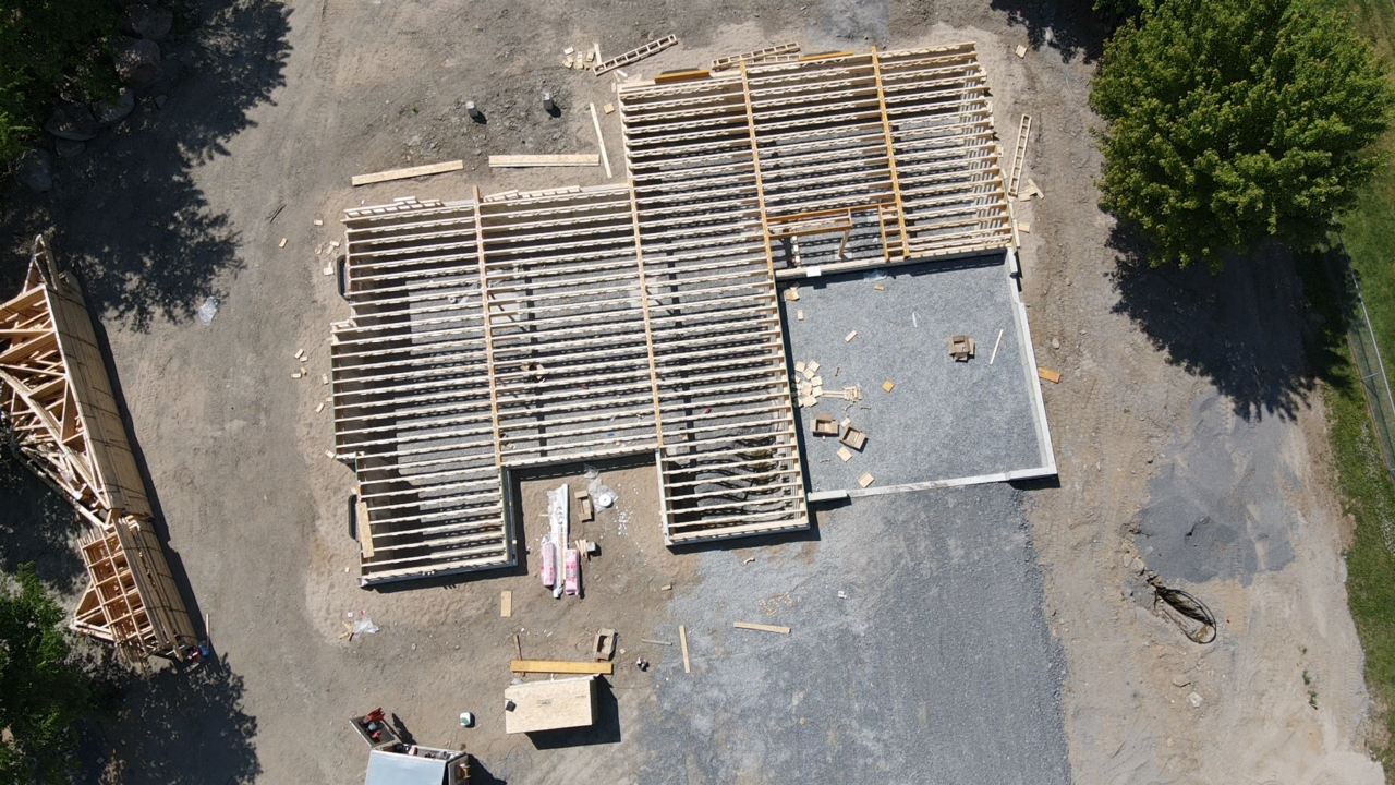 Vue aérienne de palettes en bois empilées et de matériaux de construction sur un terrain gravillonné à proximité d'arbres
