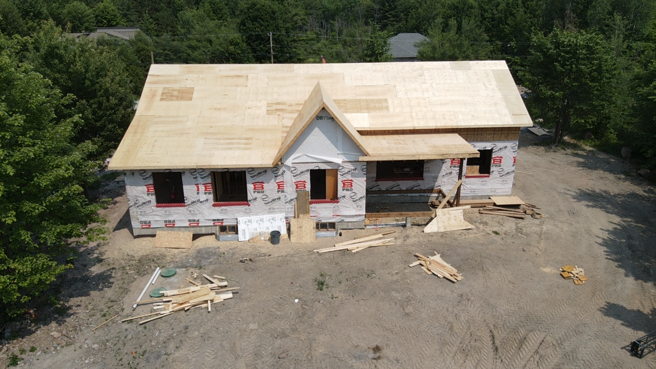 Maison partiellement construite avec revêtement apparent et toit inachevé dans une clairière boisée