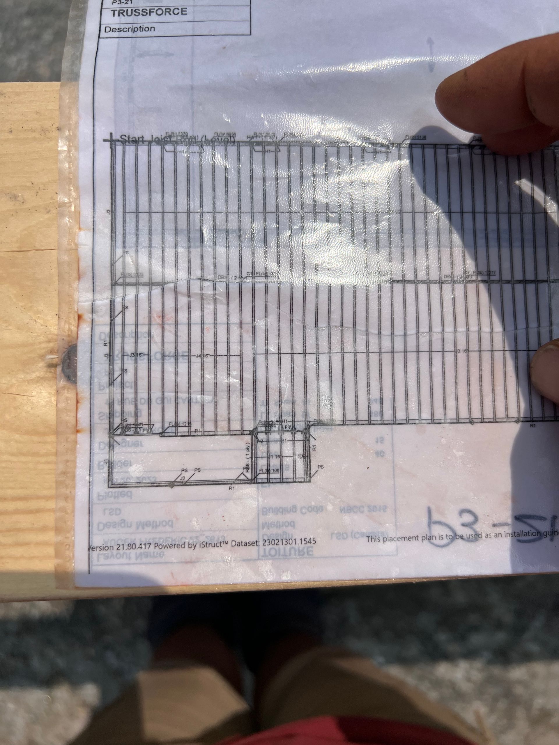 Main tenant une feuille de papier sur laquelle figure un dessin technique flou ou un plan d'étage, posée sur une surface en bois.