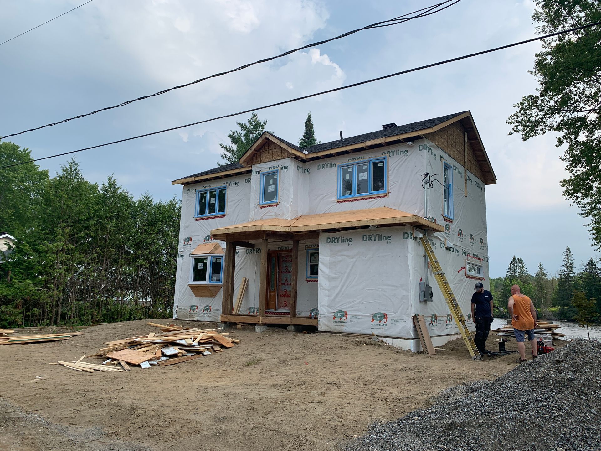 Maison à deux étages en construction avec deux ouvriers et des tas de matériaux de construction à l'extérieur
