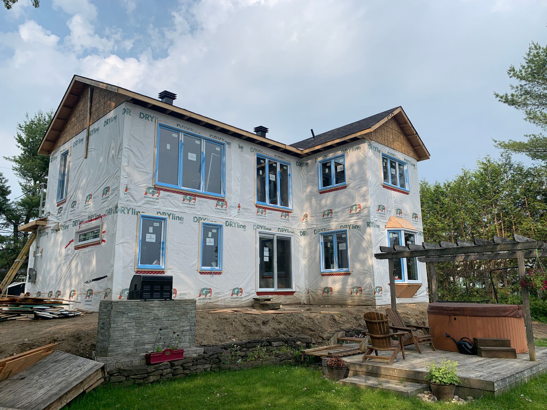 Maison à deux étages en construction, avec façade blanche, encadrements de fenêtres bleus et extérieur inachevé.