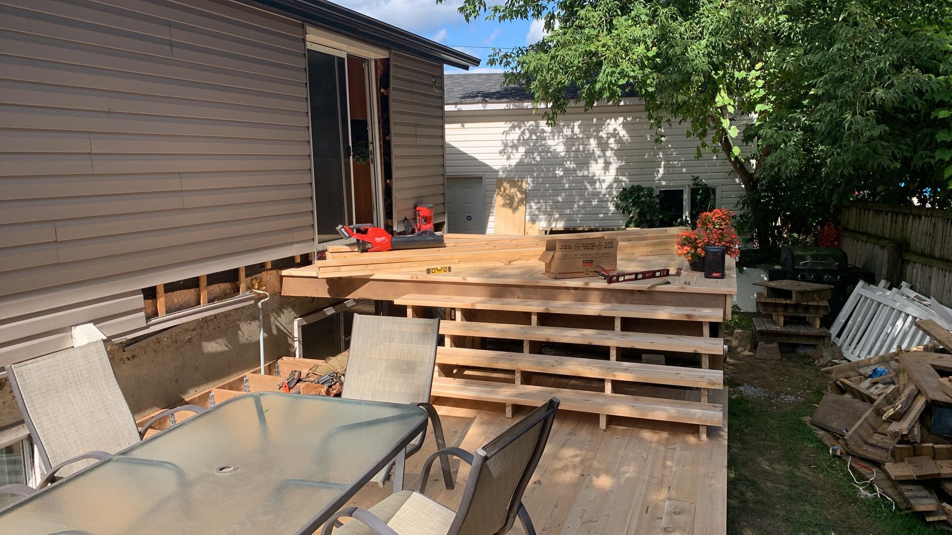 Terrasse arrière avec des palettes en bois empilées, une table et des chaises, et l'extérieur d'une maison en arrière-plan