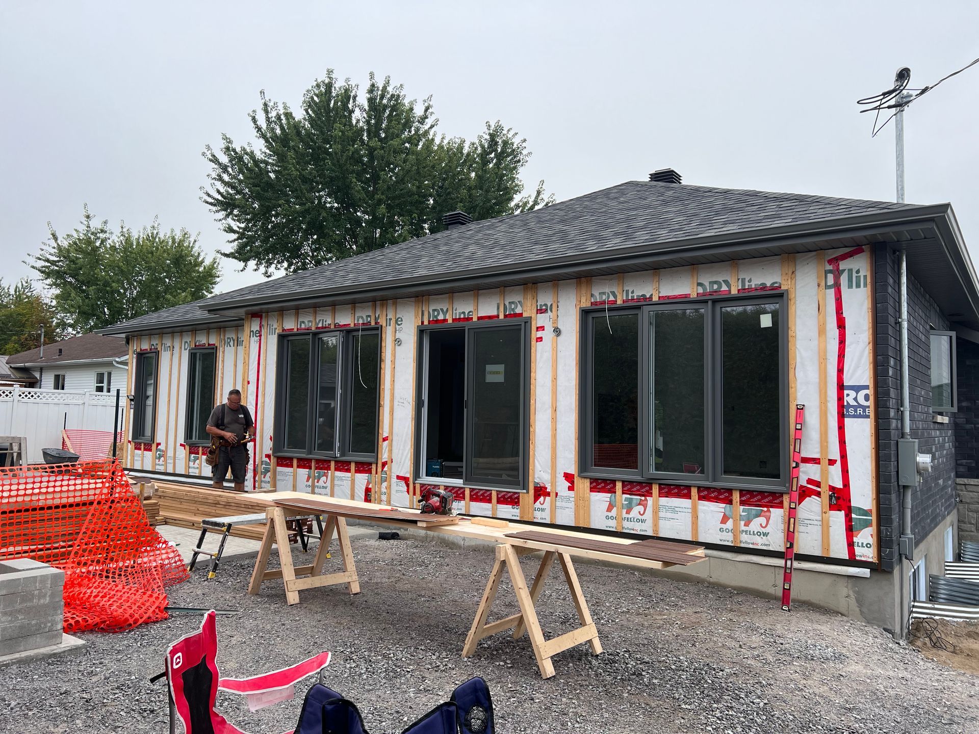 Maison de plain-pied en rénovation avec isolation apparente, barrières rouges et tables de travail devant.
