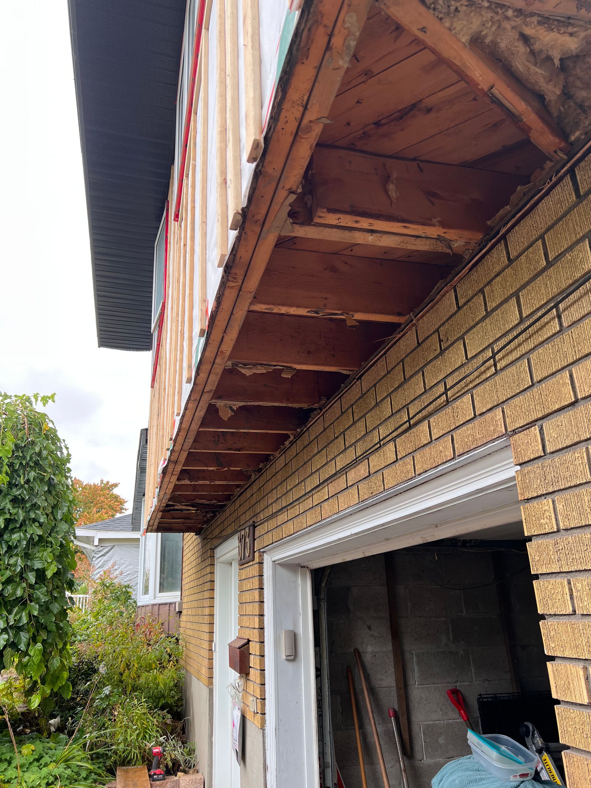 Gros plan sur l'avant-toit d'une maison en briques avec un soffite en bois apparent au-dessus d'une porte de garage ouverte