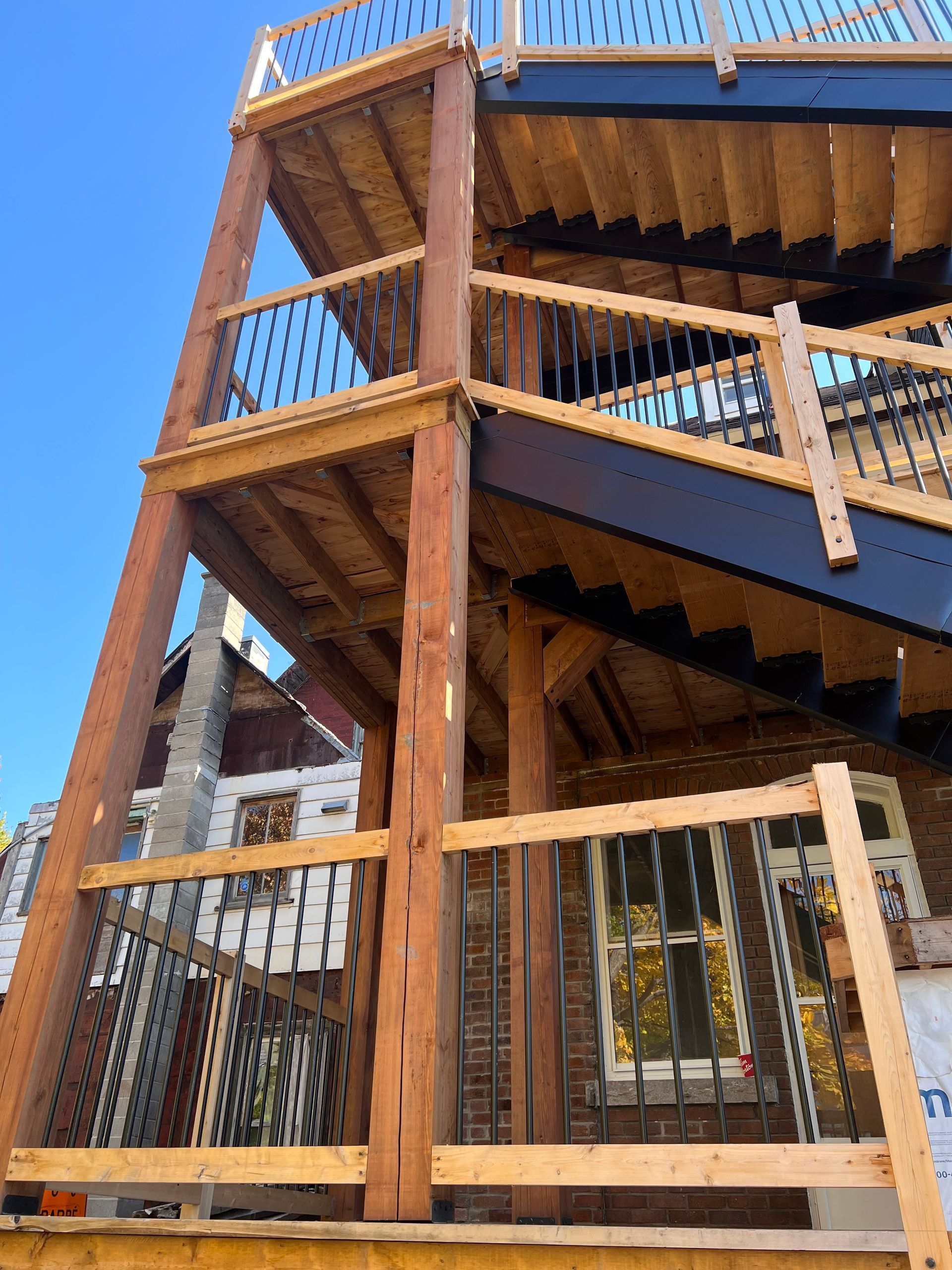 Escalier extérieur en bois et terrasse avec rambarde sur un bâtiment sous un ciel bleu clair