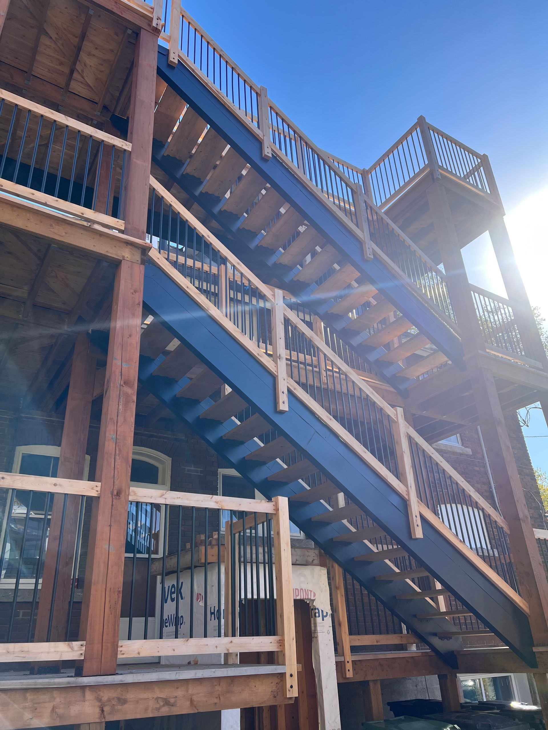 Escalier extérieur en bois avec rampes bleues, jouxtant un bâtiment délabré baigné de soleil.