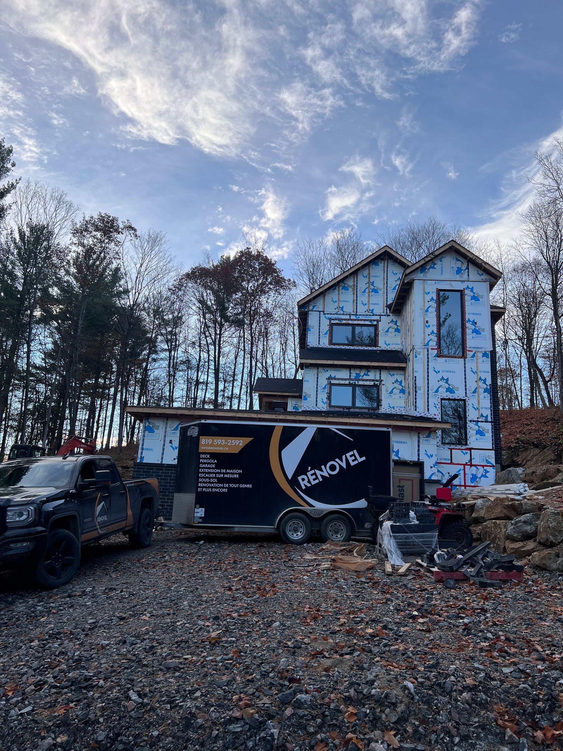 Maison à deux étages avec un camion de déménagement et une camionnette garés devant, sous un ciel nuageux.