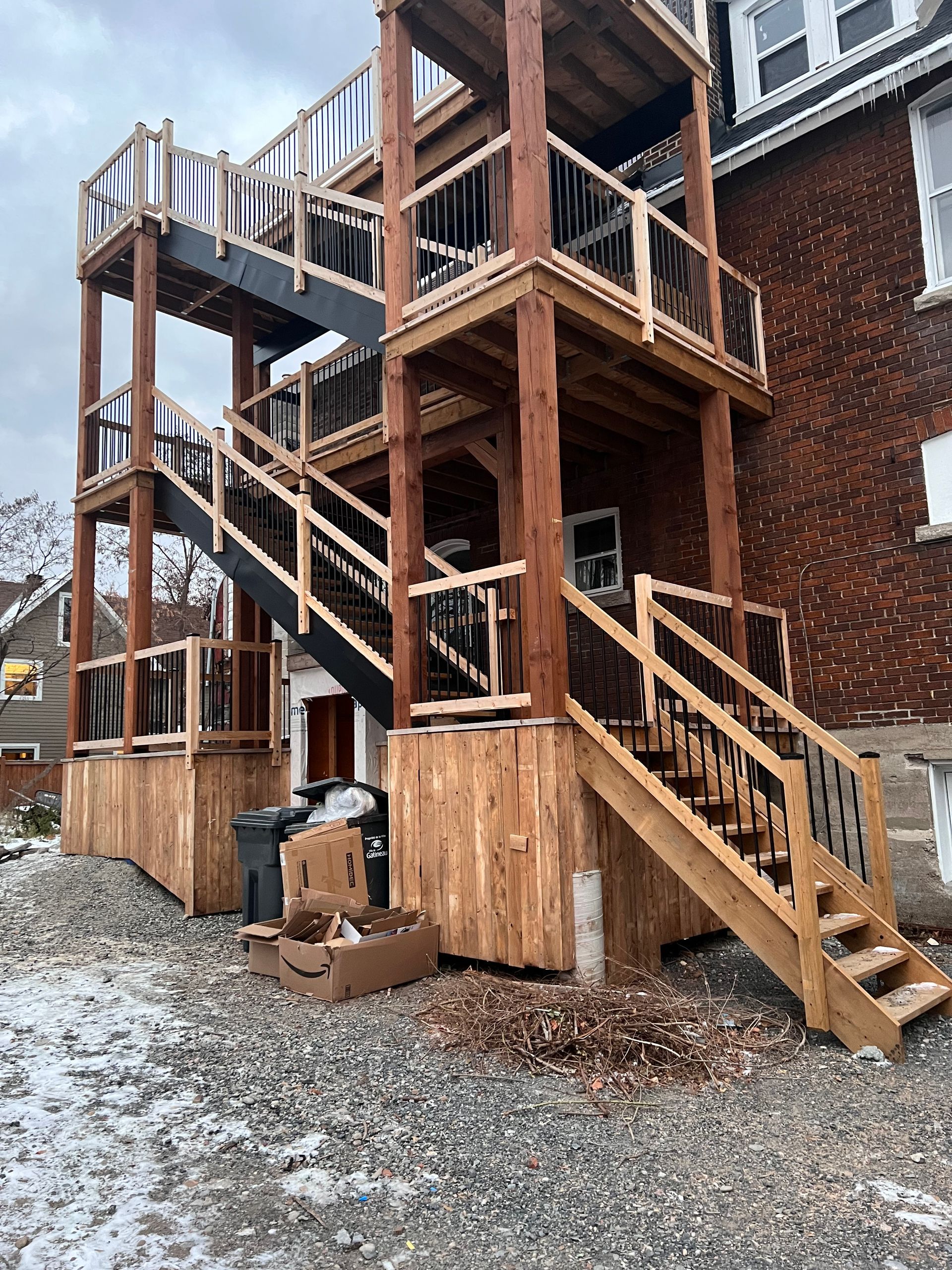 Escalier extérieur en bois et structure de terrasse à côté d'un bâtiment en briques dans une cour enneigée