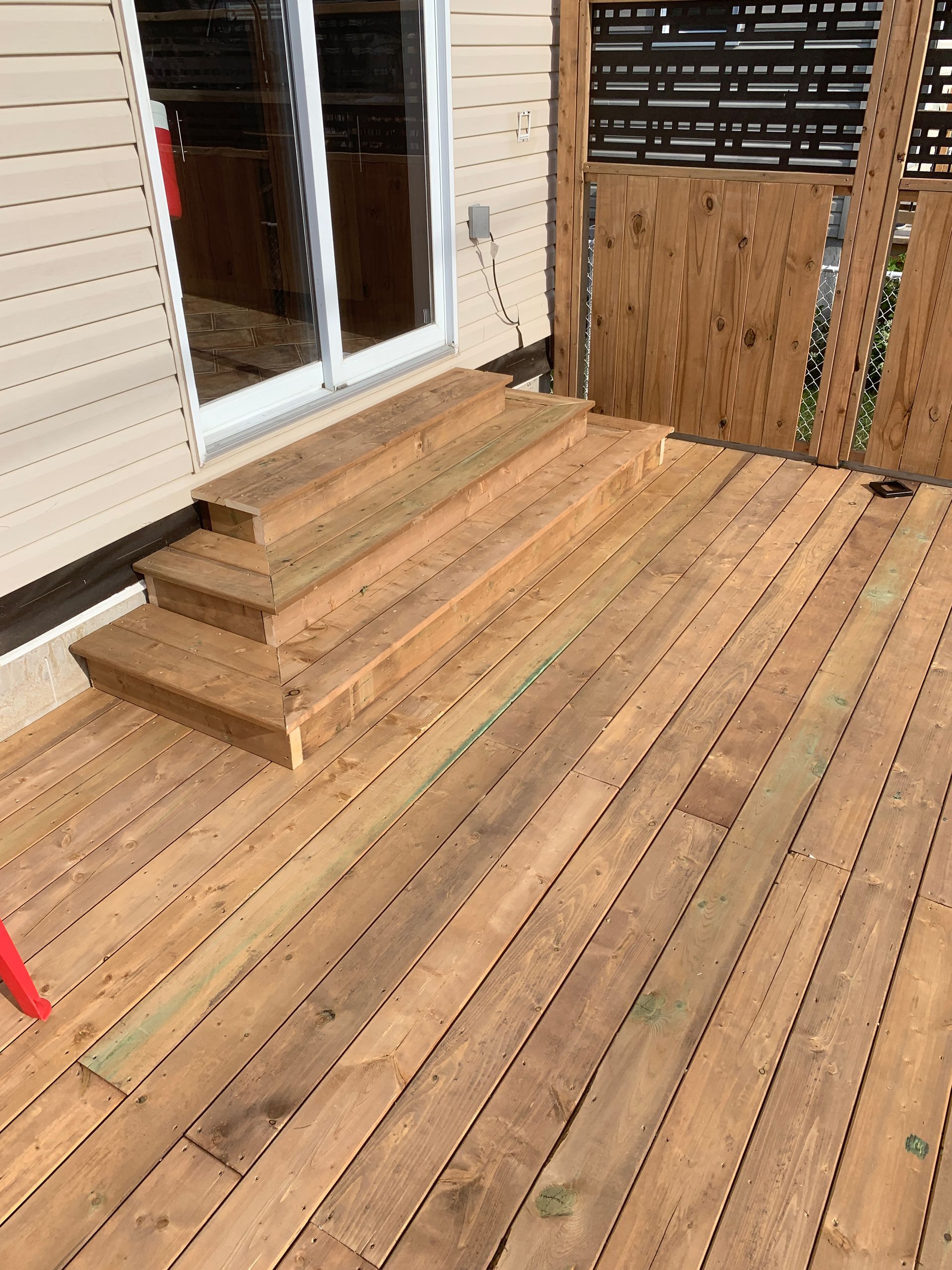 Terrasse en bois avec quelques marches menant à une porte-fenêtre coulissante et à un patio clôturé