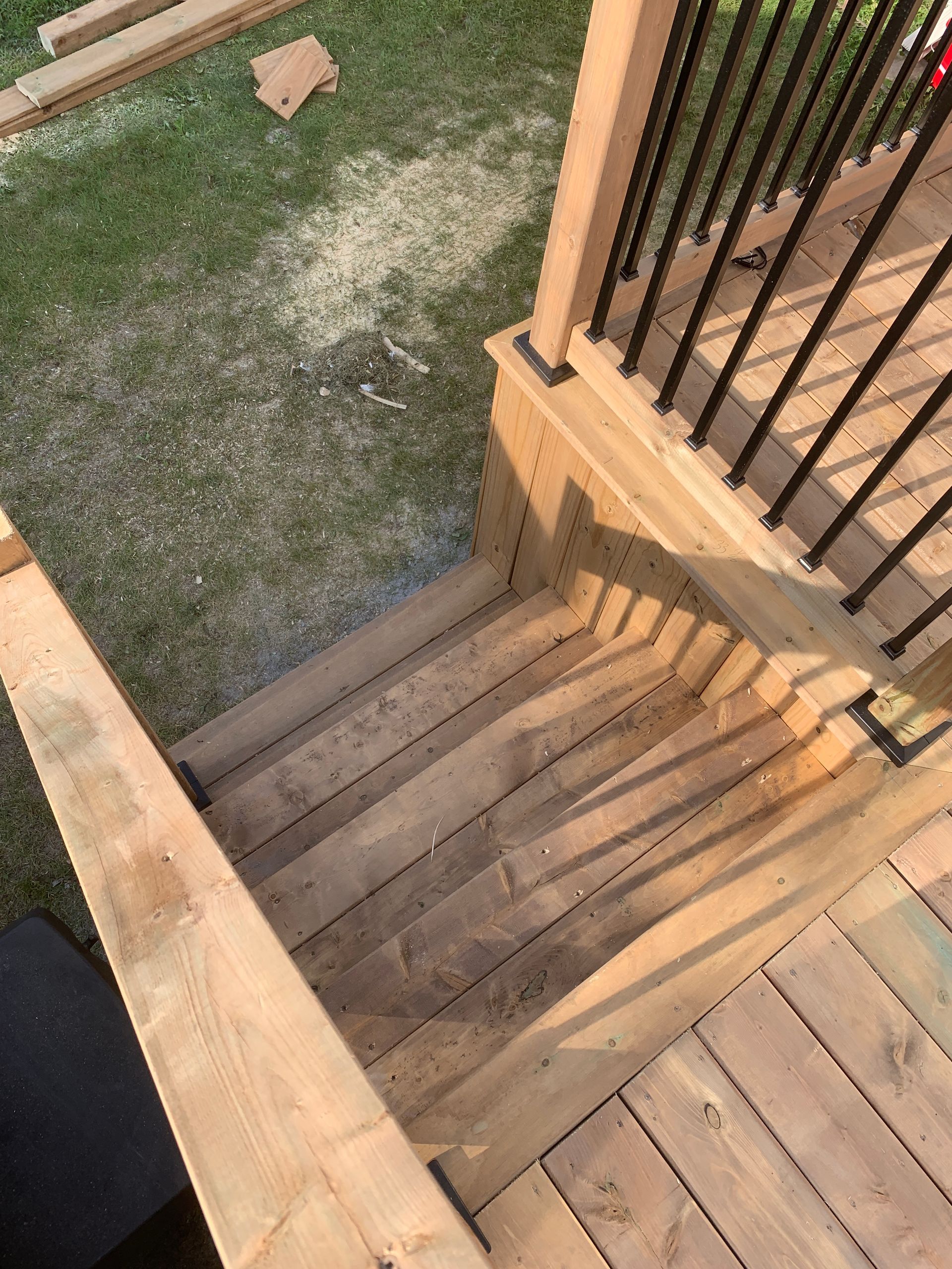 Un escalier extérieur en bois avec une rampe noire descend vers une petite pelouse.