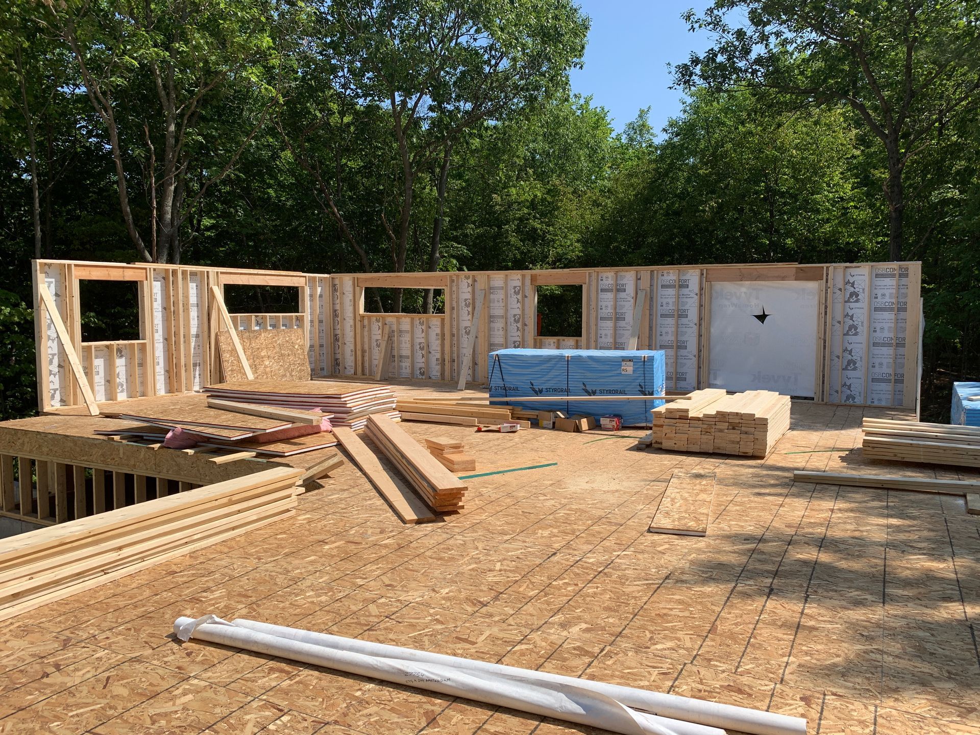 Ossature bois partiellement construite d'une maison avec contreplaqué, isolation bleue et matériaux de construction sur place