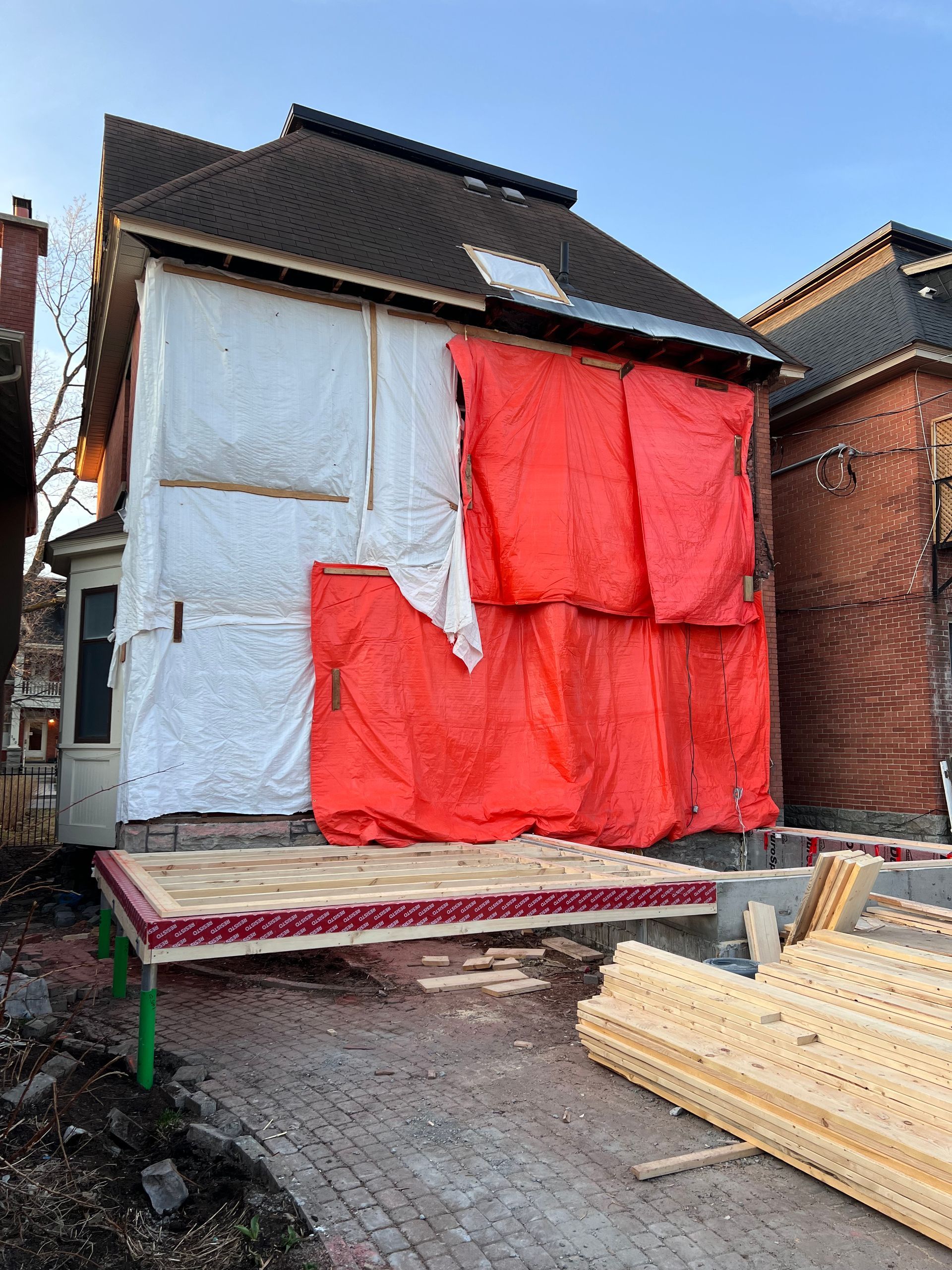 Maison en rénovation avec des bâches de protection rouges et blanches et des matériaux de construction devant.