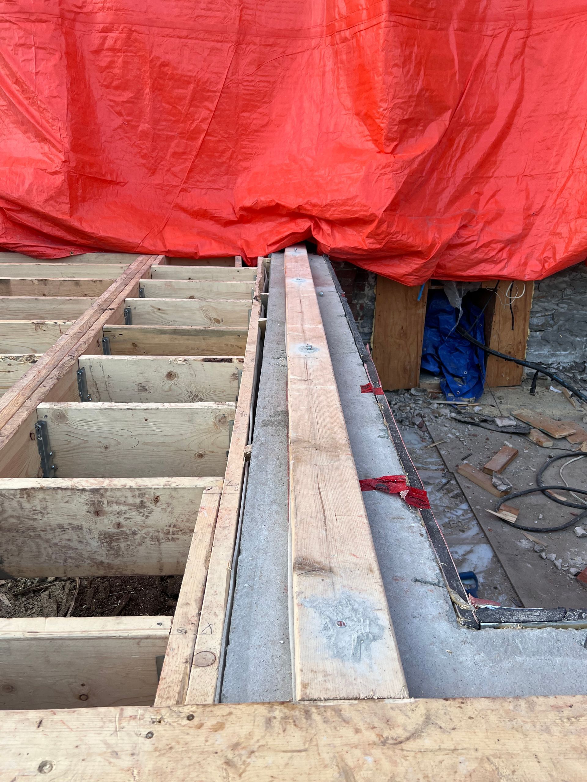 Chantier de construction avec solives apparentes, planches de bois et bâche rouge recouvrant la zone