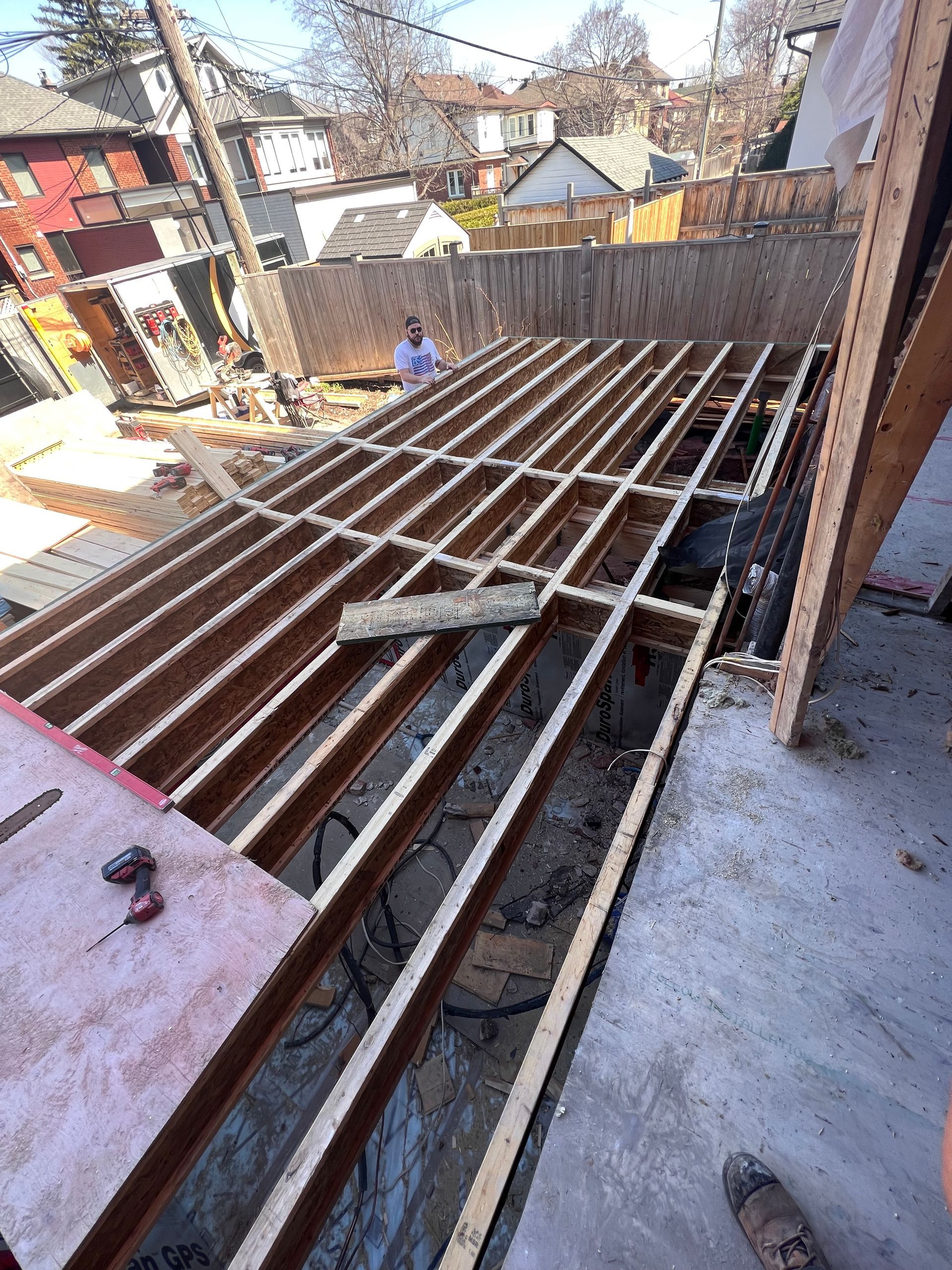 Des poutres d'acier posées sur une terrasse de toit inachevée, avec des maisons de la ville en arrière-plan.