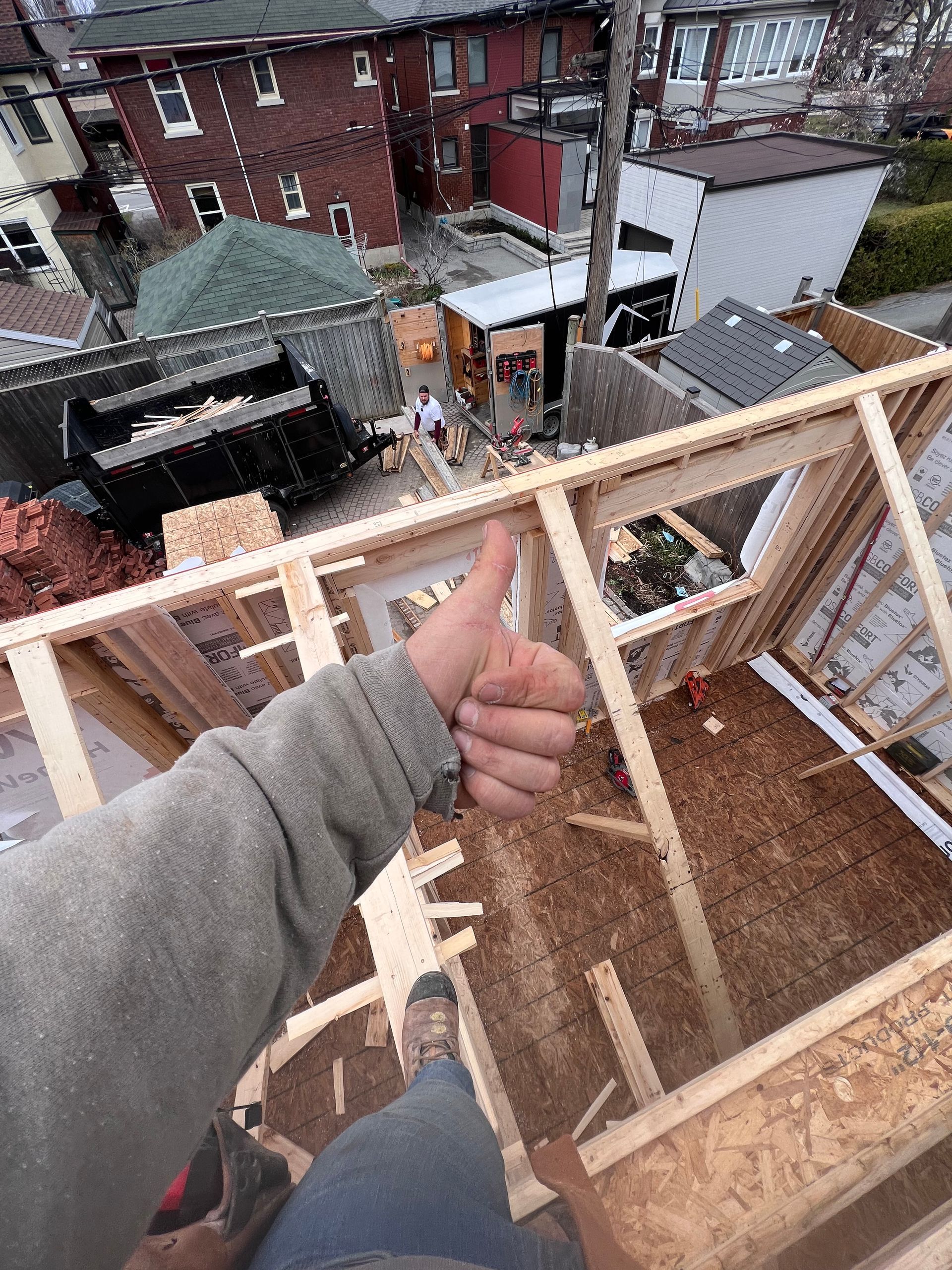 Pouce levé depuis un toit offrant une vue sur les bâtiments environnants et une personne sur une terrasse en bois.