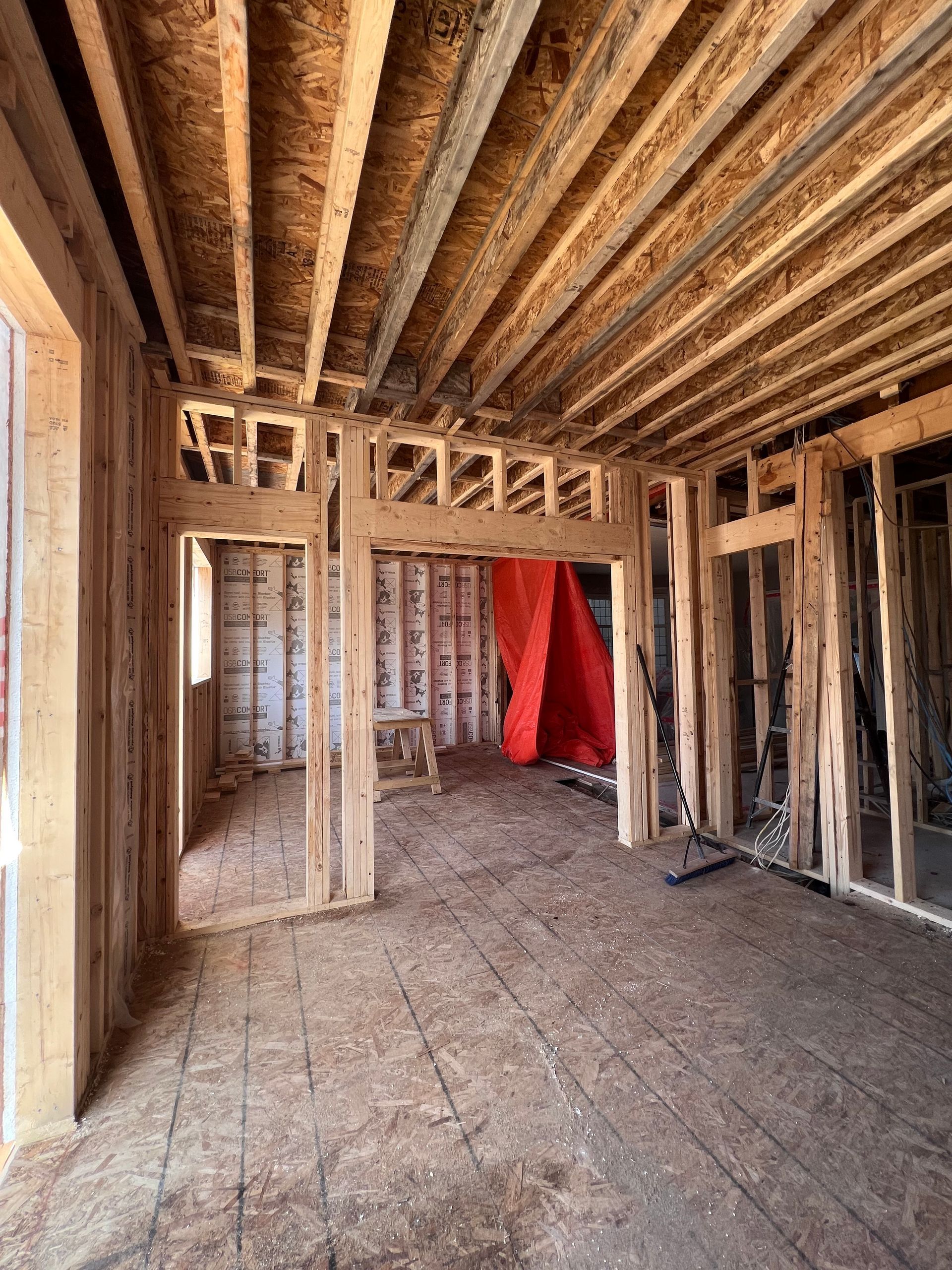 Pièce inachevée avec charpente en bois apparente, sol brut et bâche rouge devant la porte arrière.
