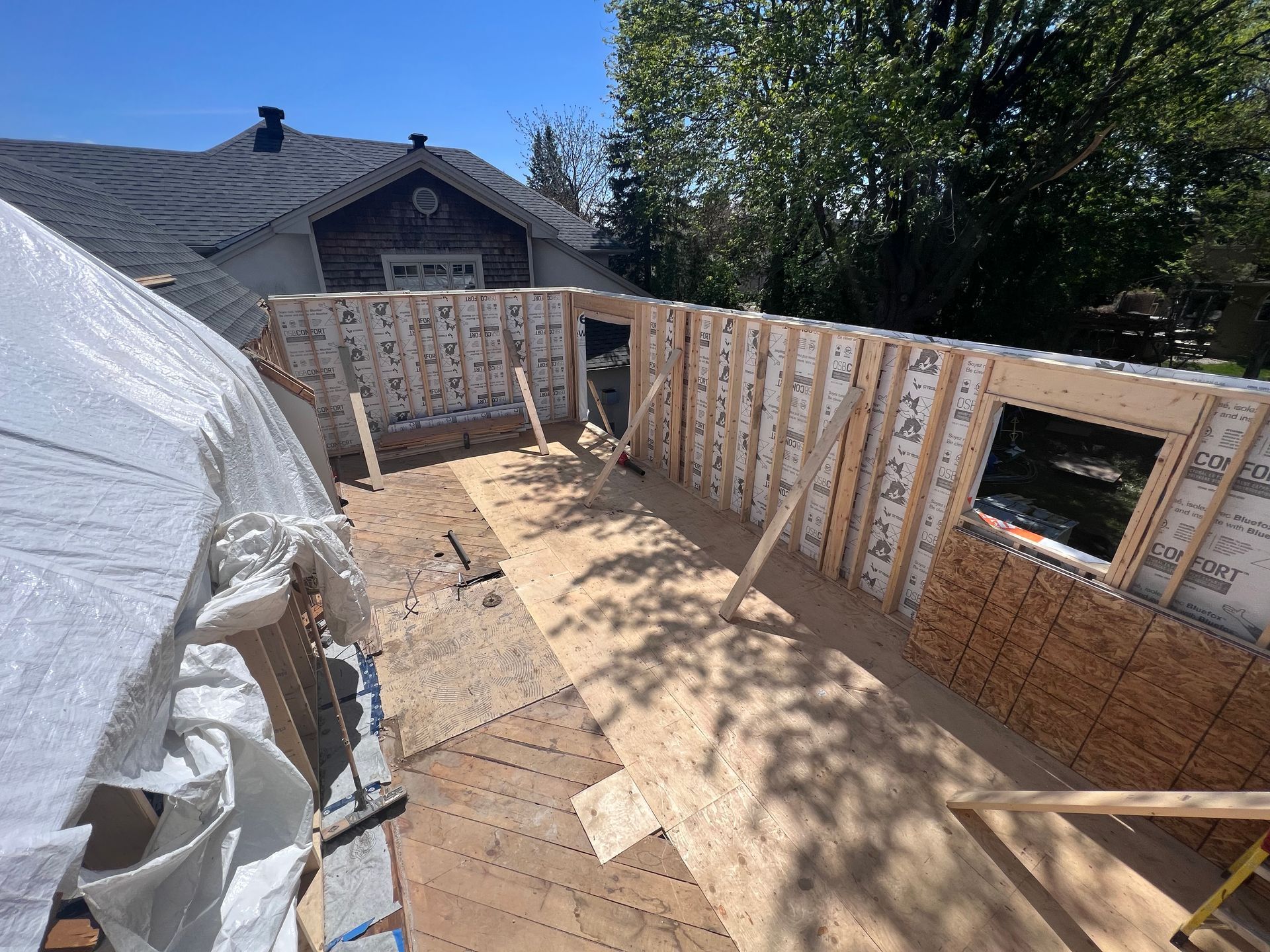 Structure en bois partiellement construite, avec des murs à ossature et un toit ouvert, en cours de construction dans une cour arrière ensoleillée.