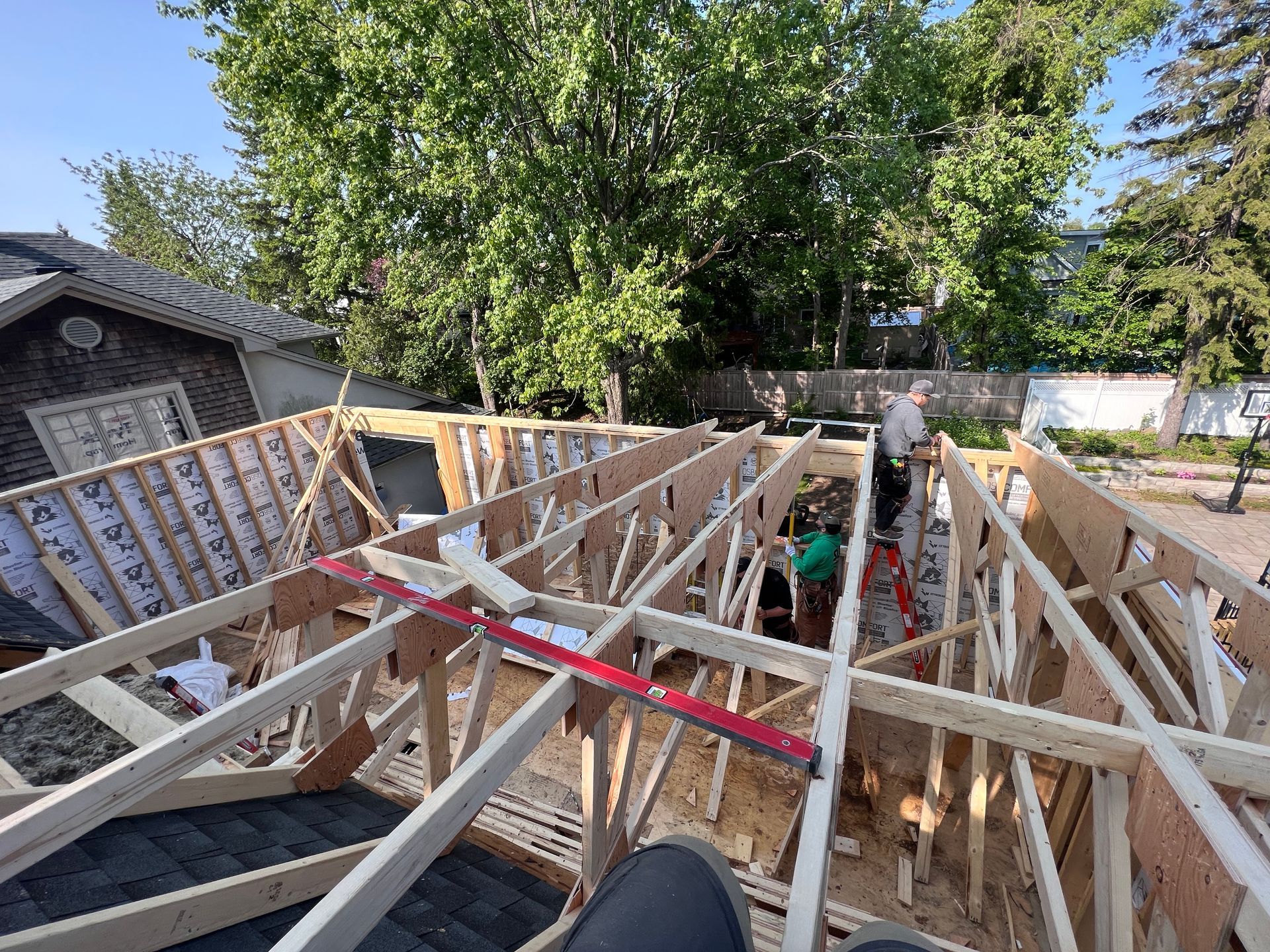 Charpente d'une maison en construction, avec fermes et poutres en bois, dans une cour arrière, vue en plein jour.