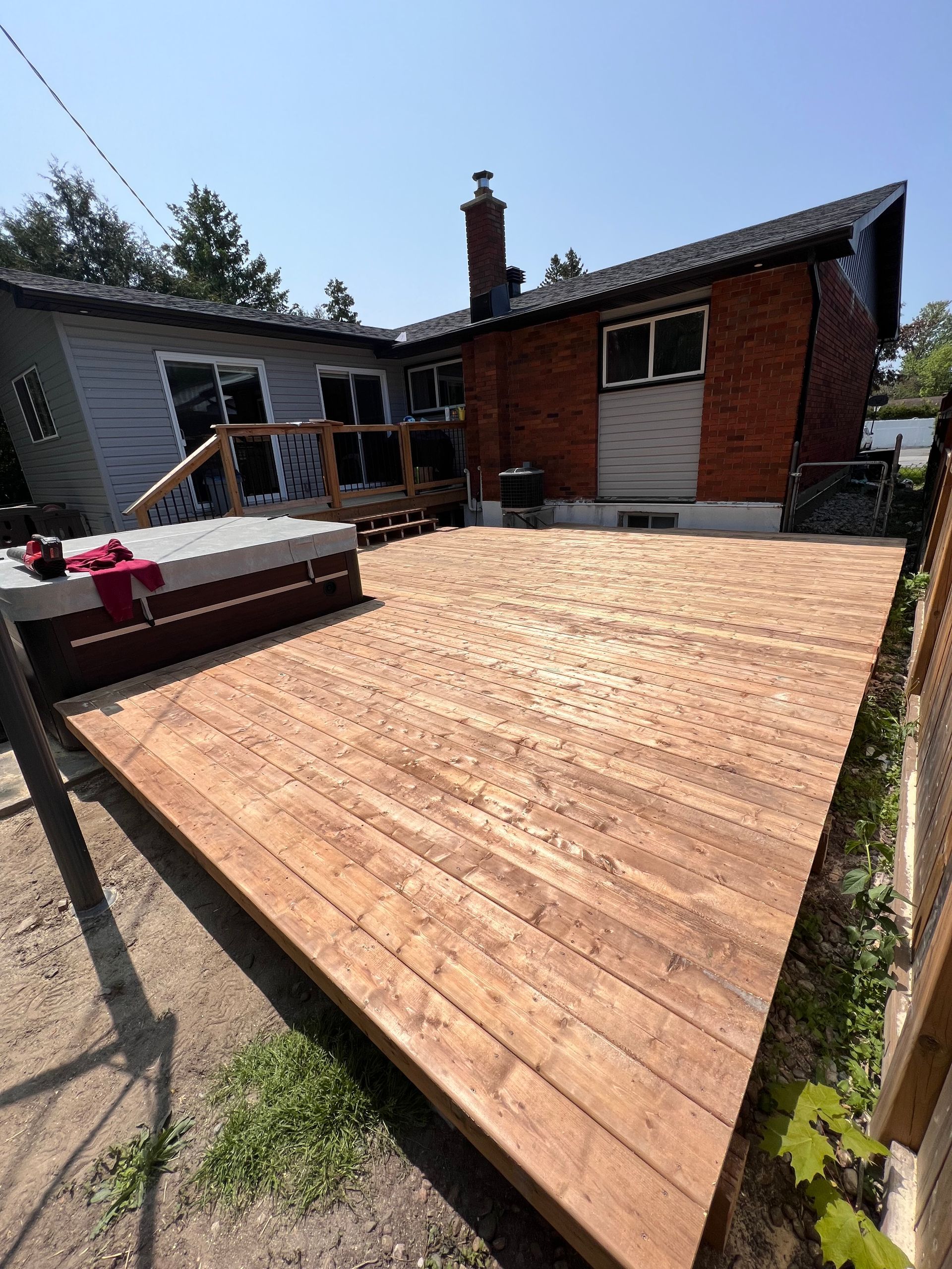 Terrasse en bois en construction à l'arrière d'une maison en briques, avec mobilier de jardin et cheminée.