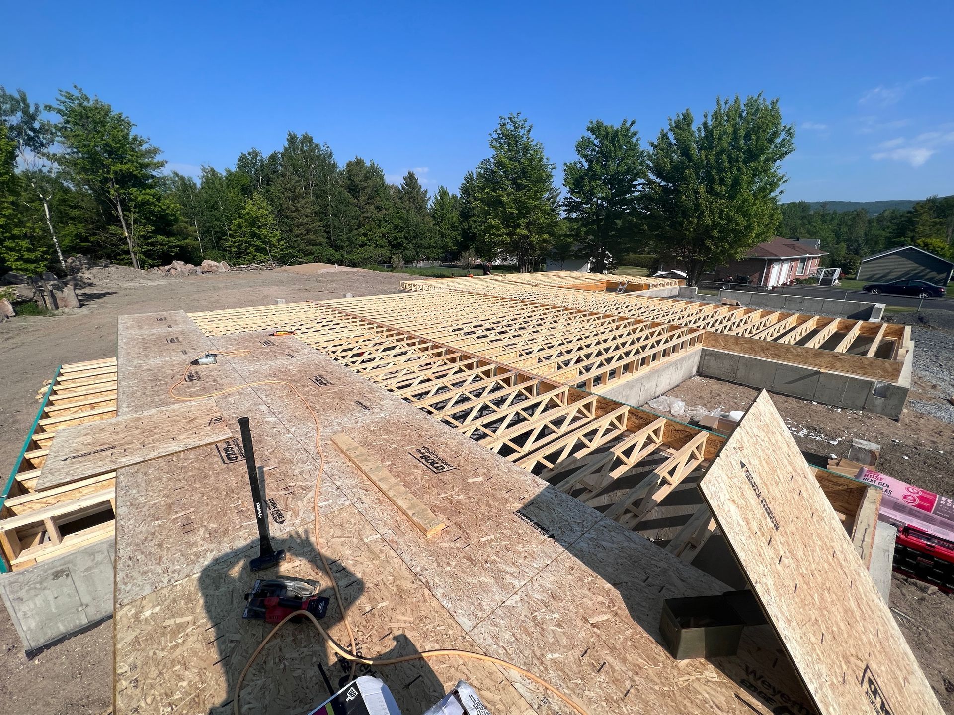 Fondations de maison en construction avec ossature de plancher en bois sur un terrain dégagé, arbres en arrière-plan