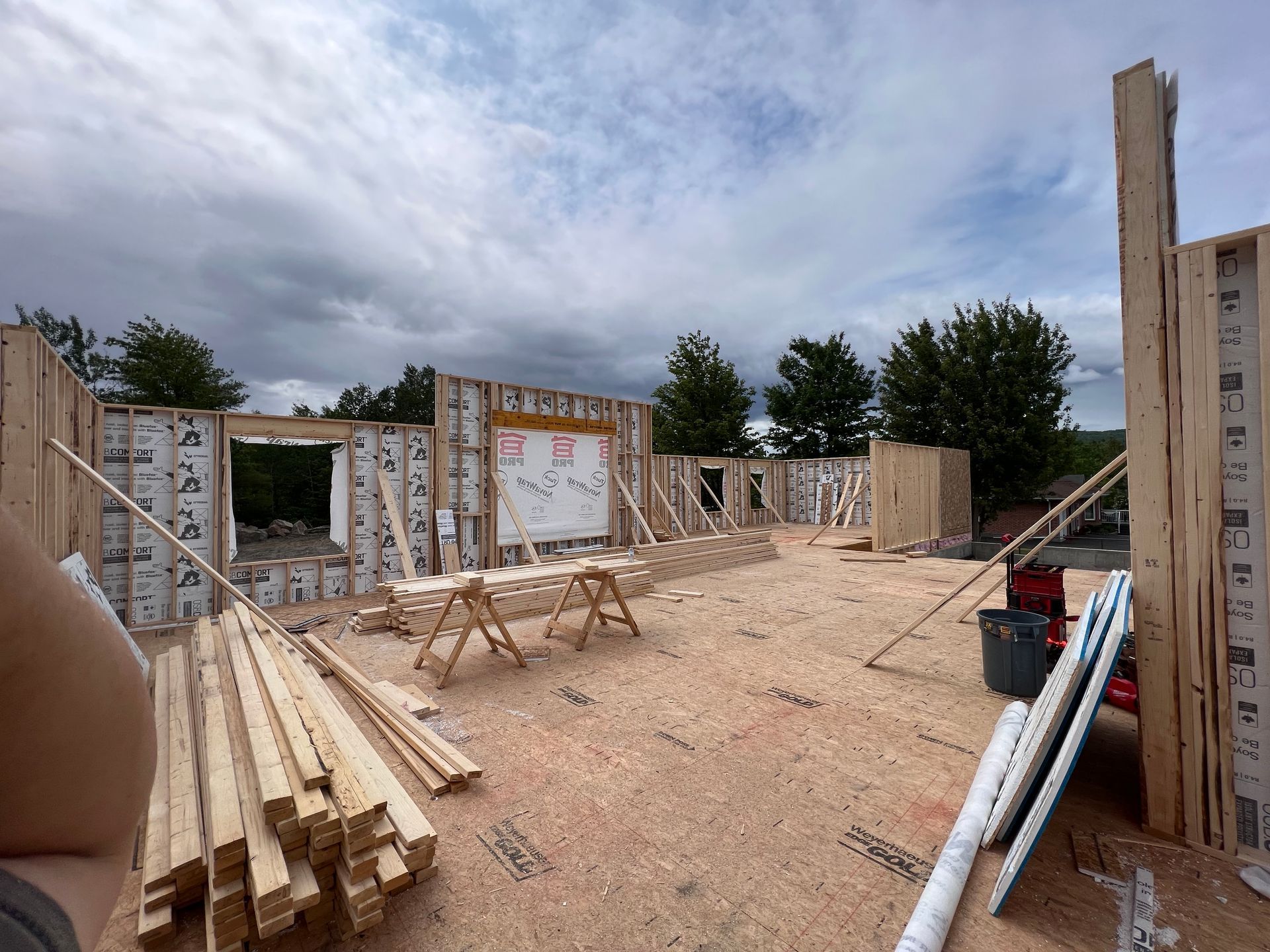 Chantier de construction avec des murs à ossature bois, des piles de bois et des outils sous un ciel nuageux