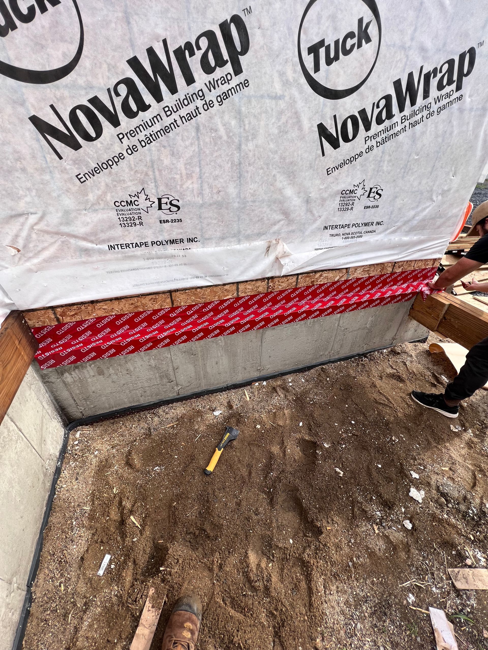 Mur de chantier recouvert de NovaWrap blanc, avec des solins rouges et de la terre apparente en dessous.