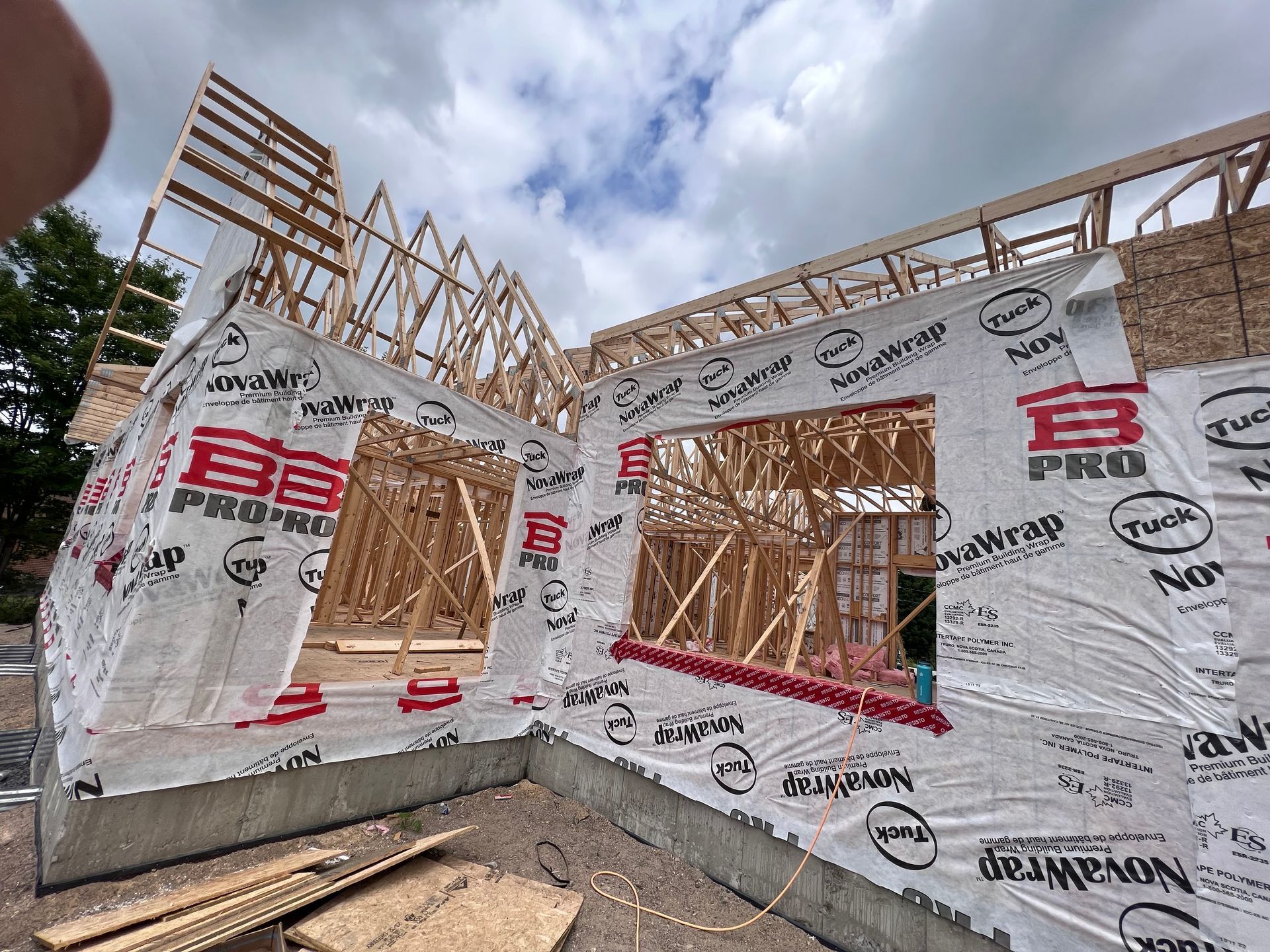 Maison partiellement en construction, avec murs extérieurs recouverts d'un revêtement et ouvertures pour fenêtres et portes.