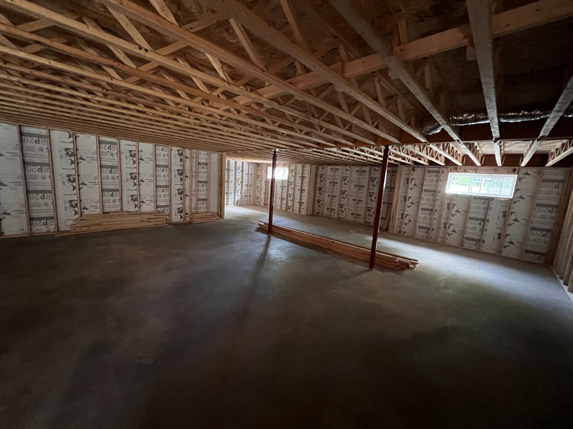 Sous-sol non aménagé avec solives de plafond en bois apparentes, murs isolés et sol en béton.