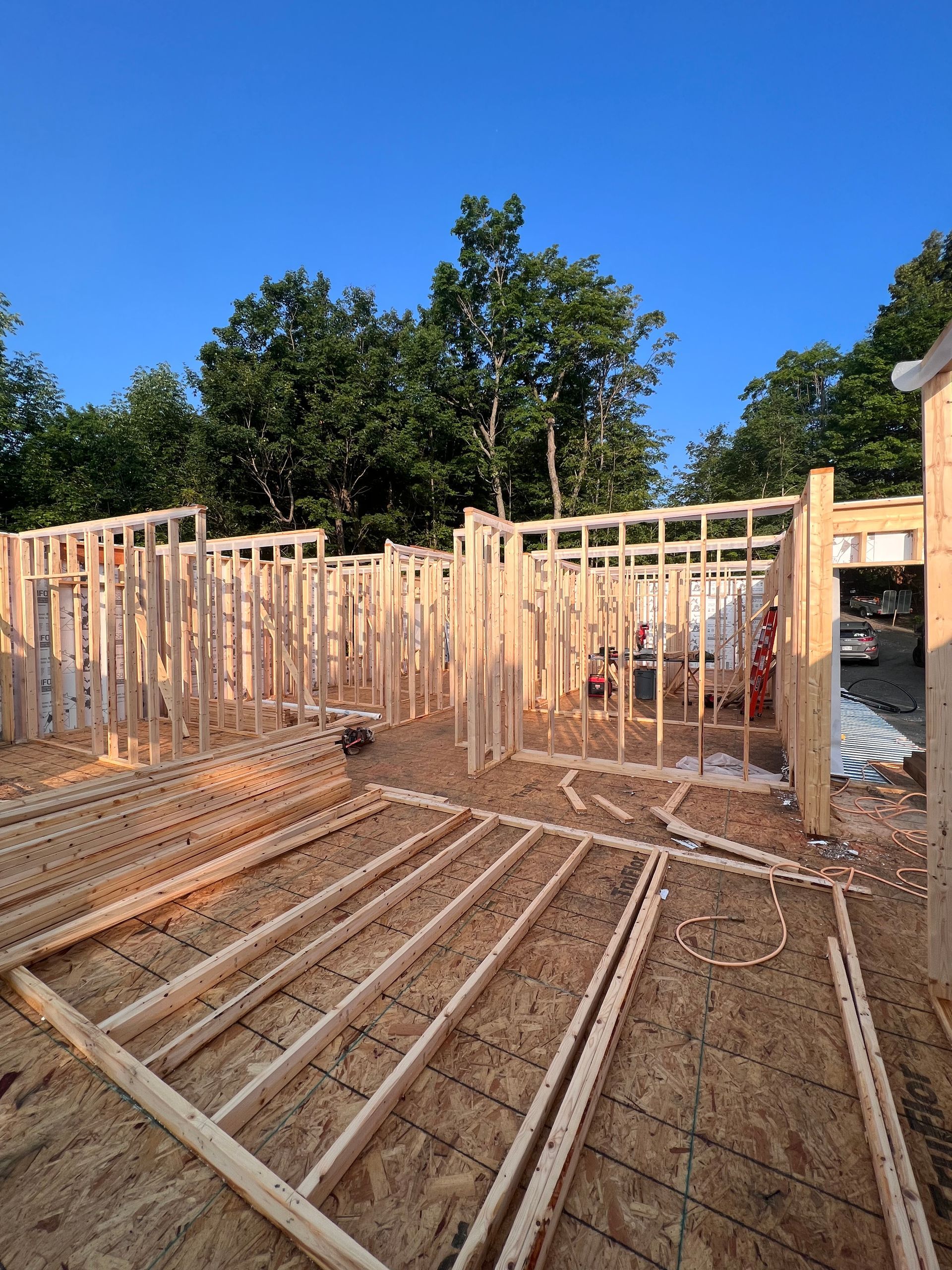 Maison à ossature bois en construction, avec solives apparentes et un ciel bleu dégagé au-dessus.
