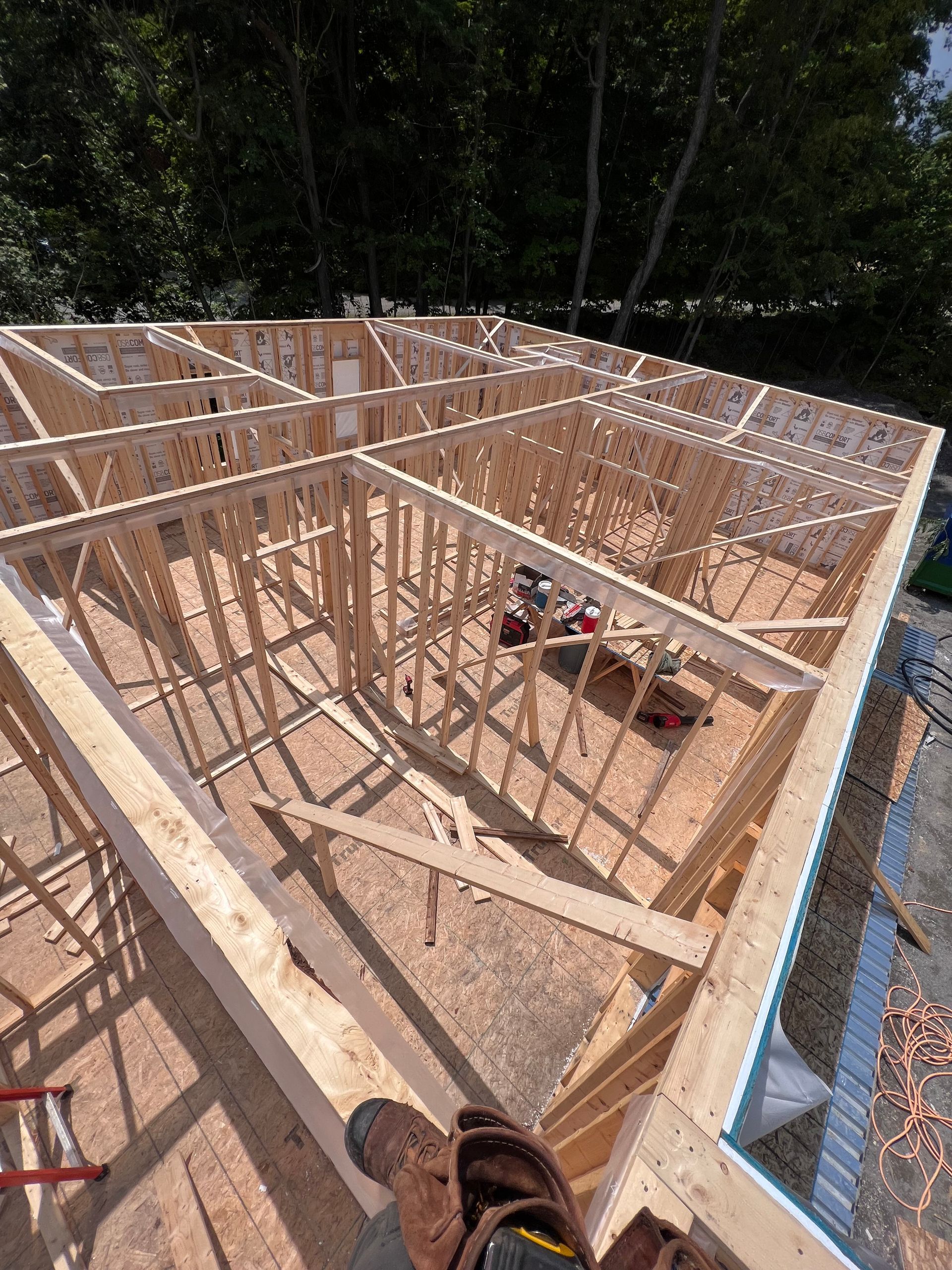 Maison à ossature bois en construction, vue de dessus, avec fermes et montants de murs apparents.