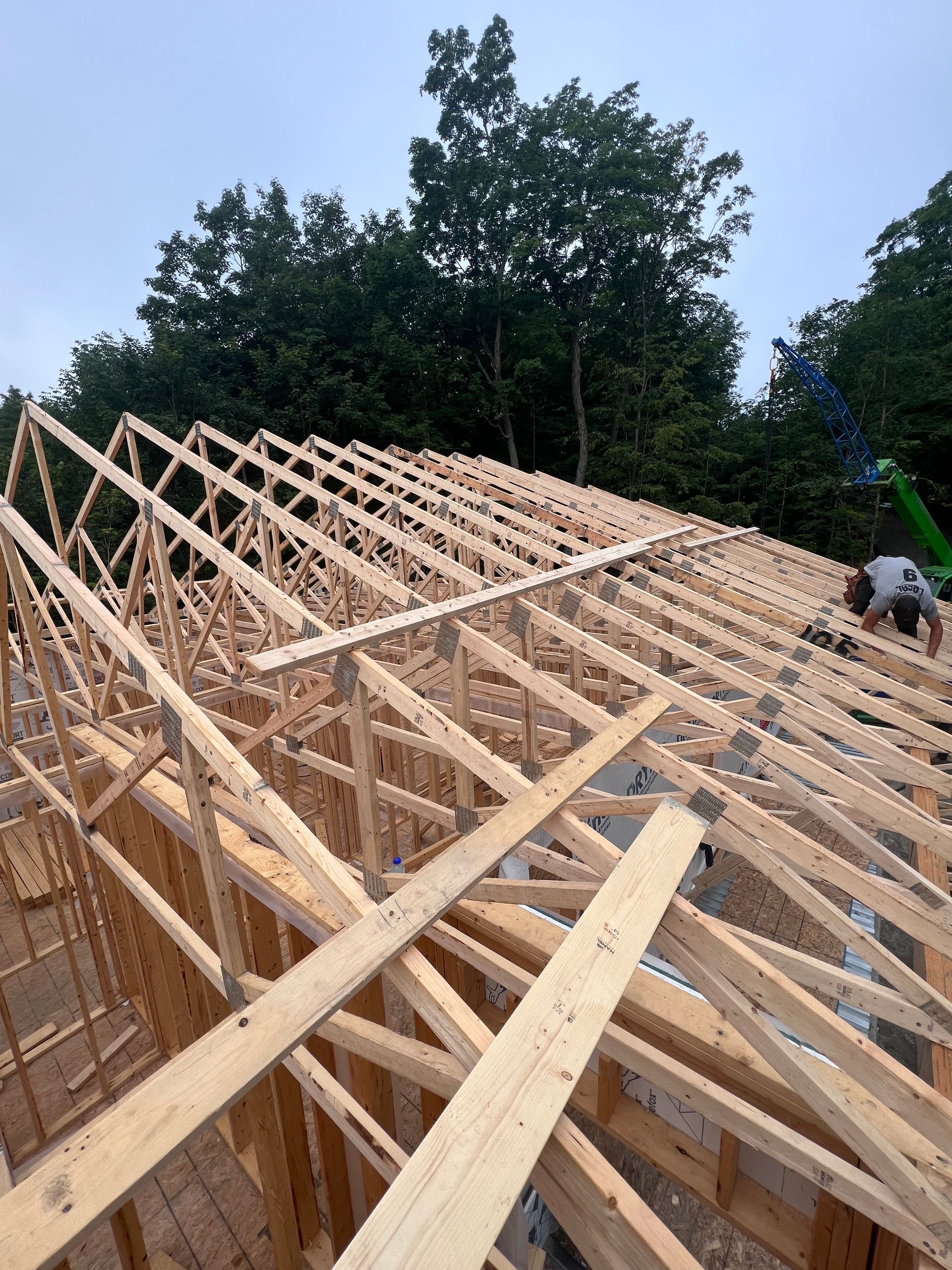 Charpente de toit en bois en cours de construction sur une ossature de maison, avec un ouvrier à droite.
