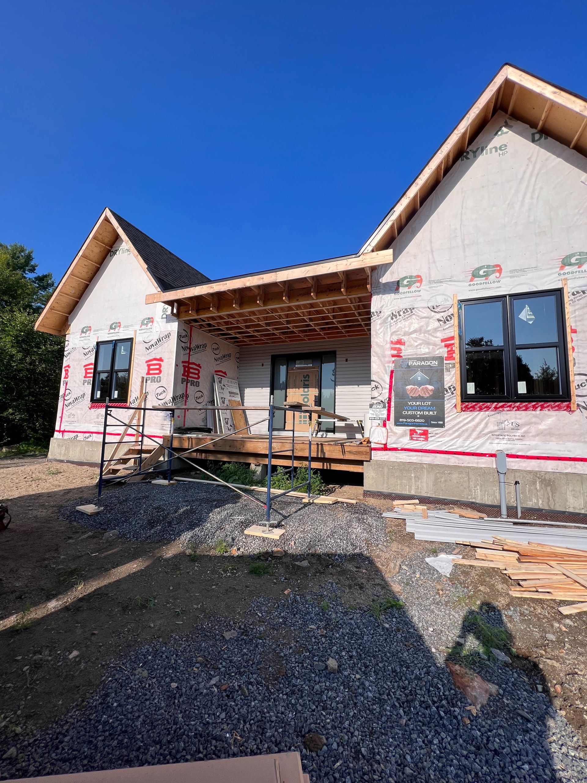 Maison neuve en construction avec charpente apparente, fenêtres et premier plan recouvert de gravier