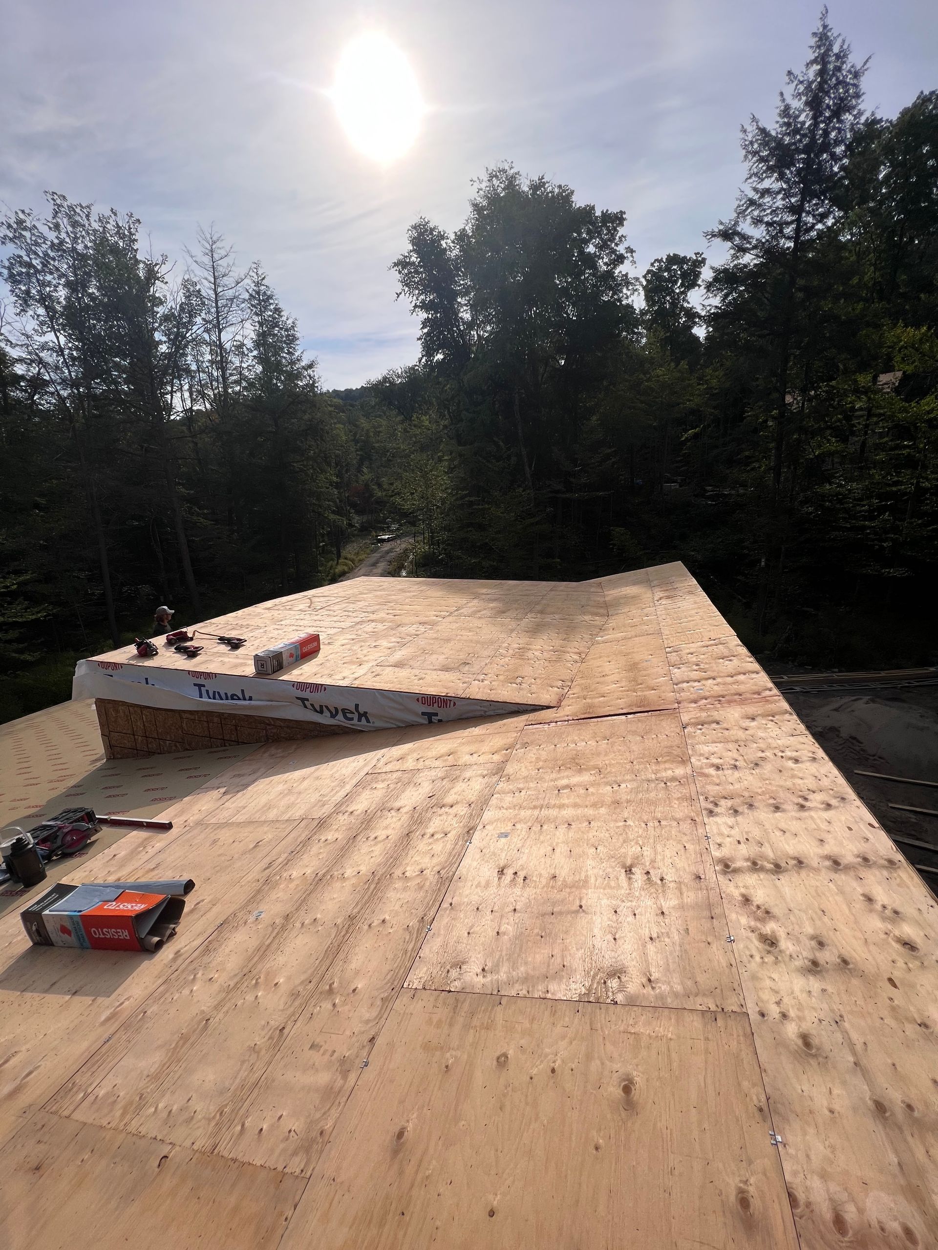Toiture en bois en construction dans une clairière, avec des outils sur le contreplaqué et la lumière du soleil au-dessus