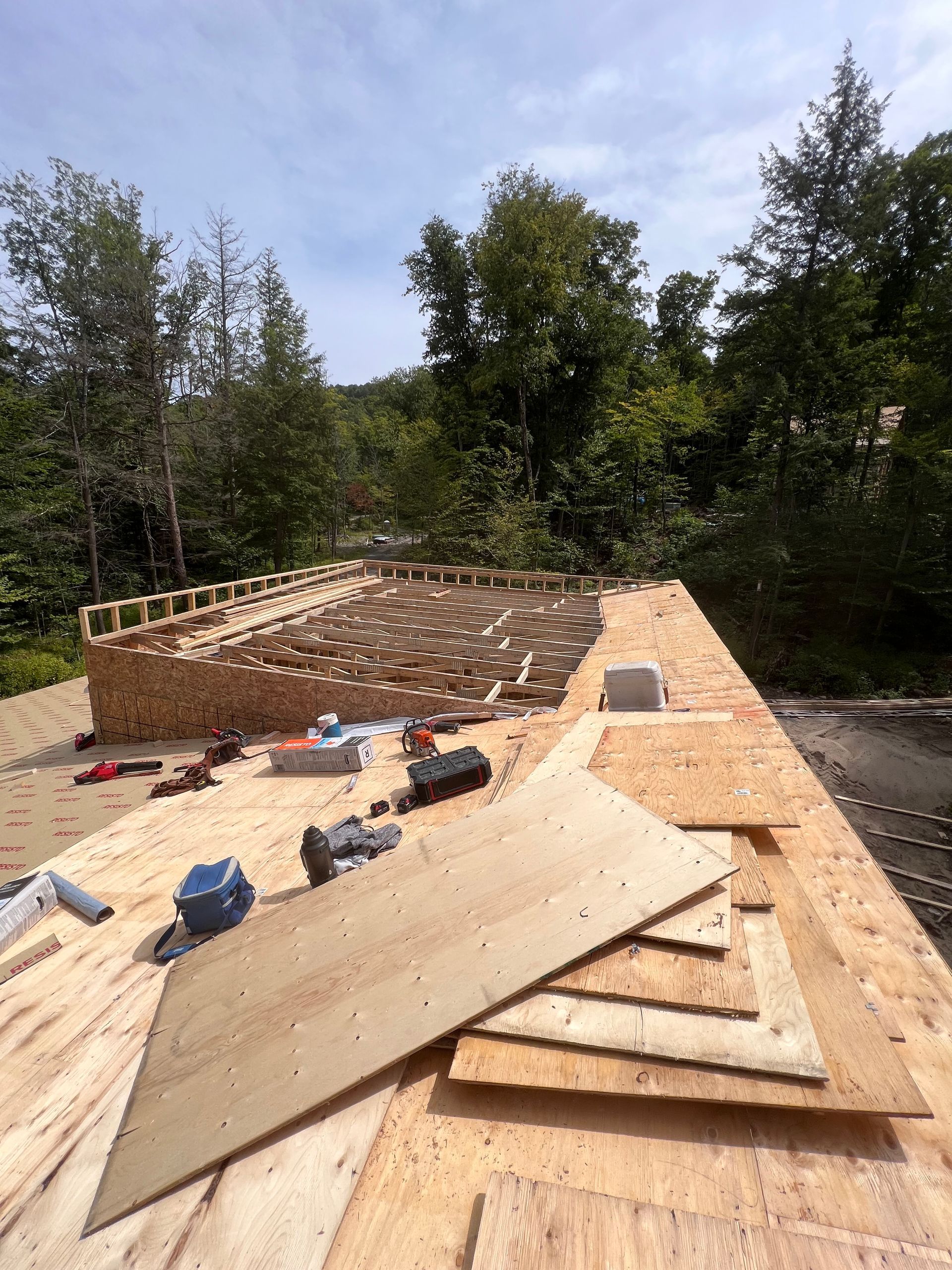 Charpente de toit en bois partiellement construite, avec des outils, sur un chantier de construction dans une zone boisée.