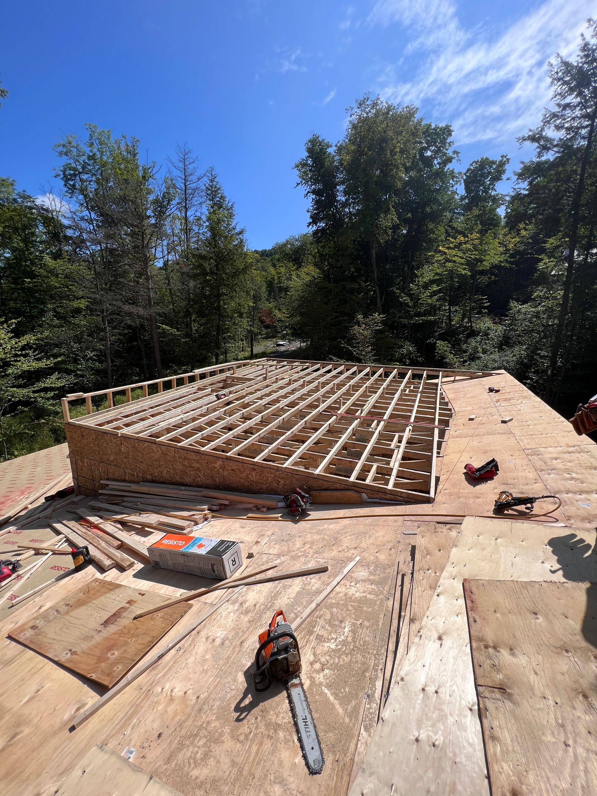 Chantier de construction avec un mur de fondation en briques et une charpente en bois sous un ciel d'un bleu éclatant