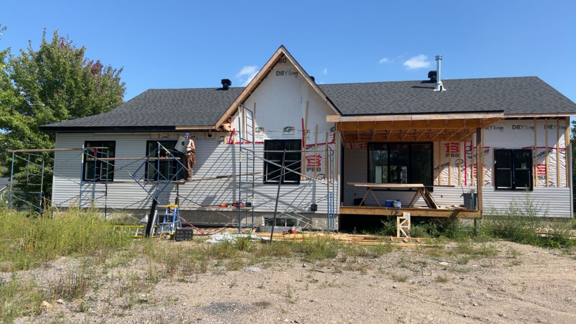 Maison de plain-pied en rénovation avec échafaudages et porche d'entrée inachevé donnant sur une cour gazonnée