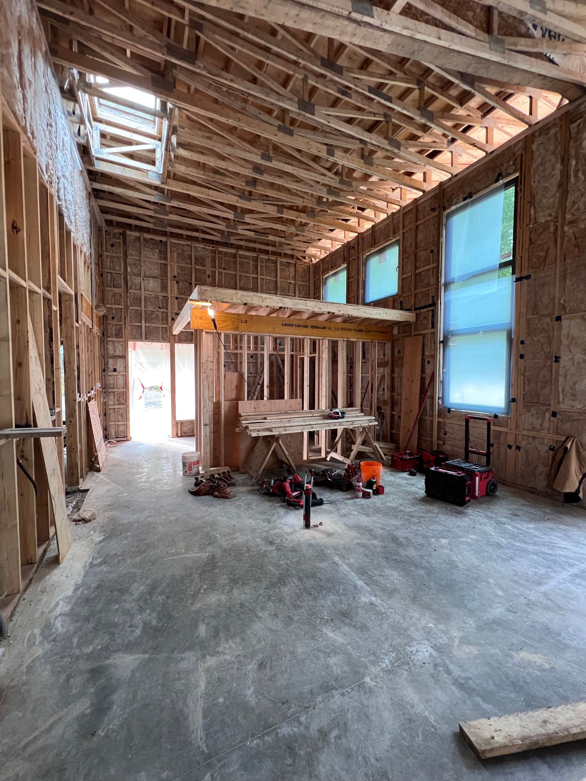 Intérieur d'une maison inachevée avec charpente apparente, sol en béton, échelles et matériaux de construction.