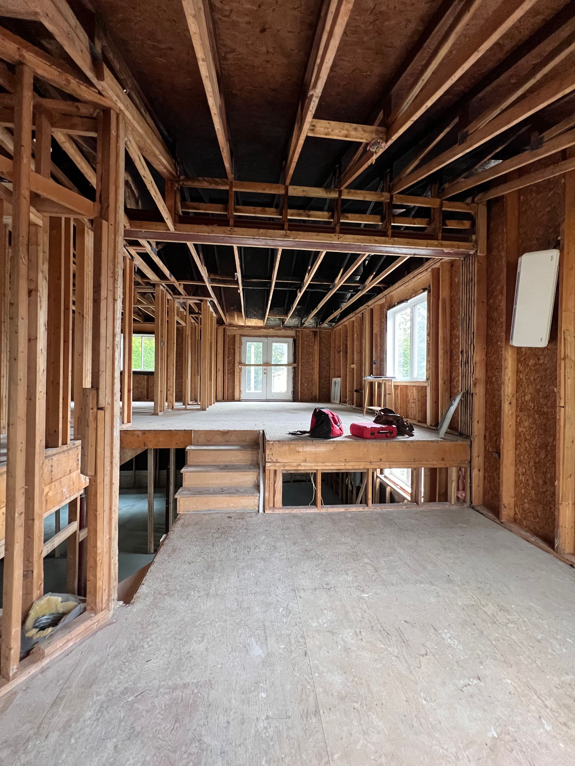 Intérieur d'une maison inachevée avec charpente en bois apparente, solives de plafond apparentes et un établi avec des outils.