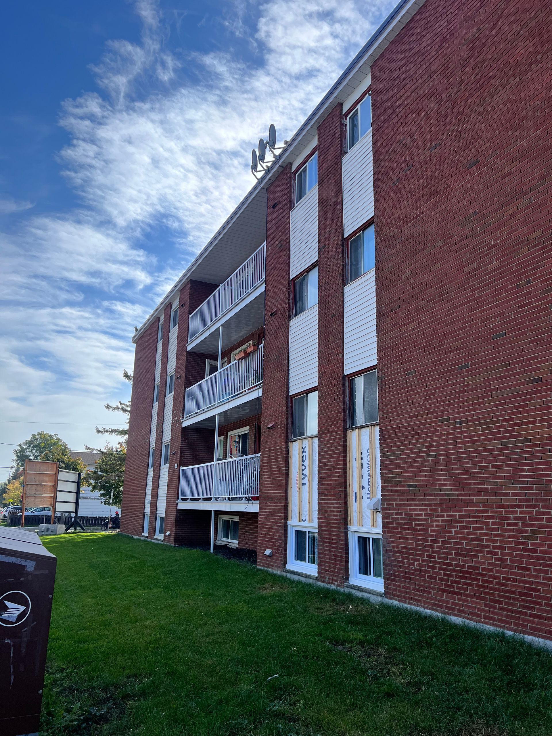 Immeuble d'appartements en briques avec balcons blancs donnant sur une pelouse sous un ciel partiellement nuageux