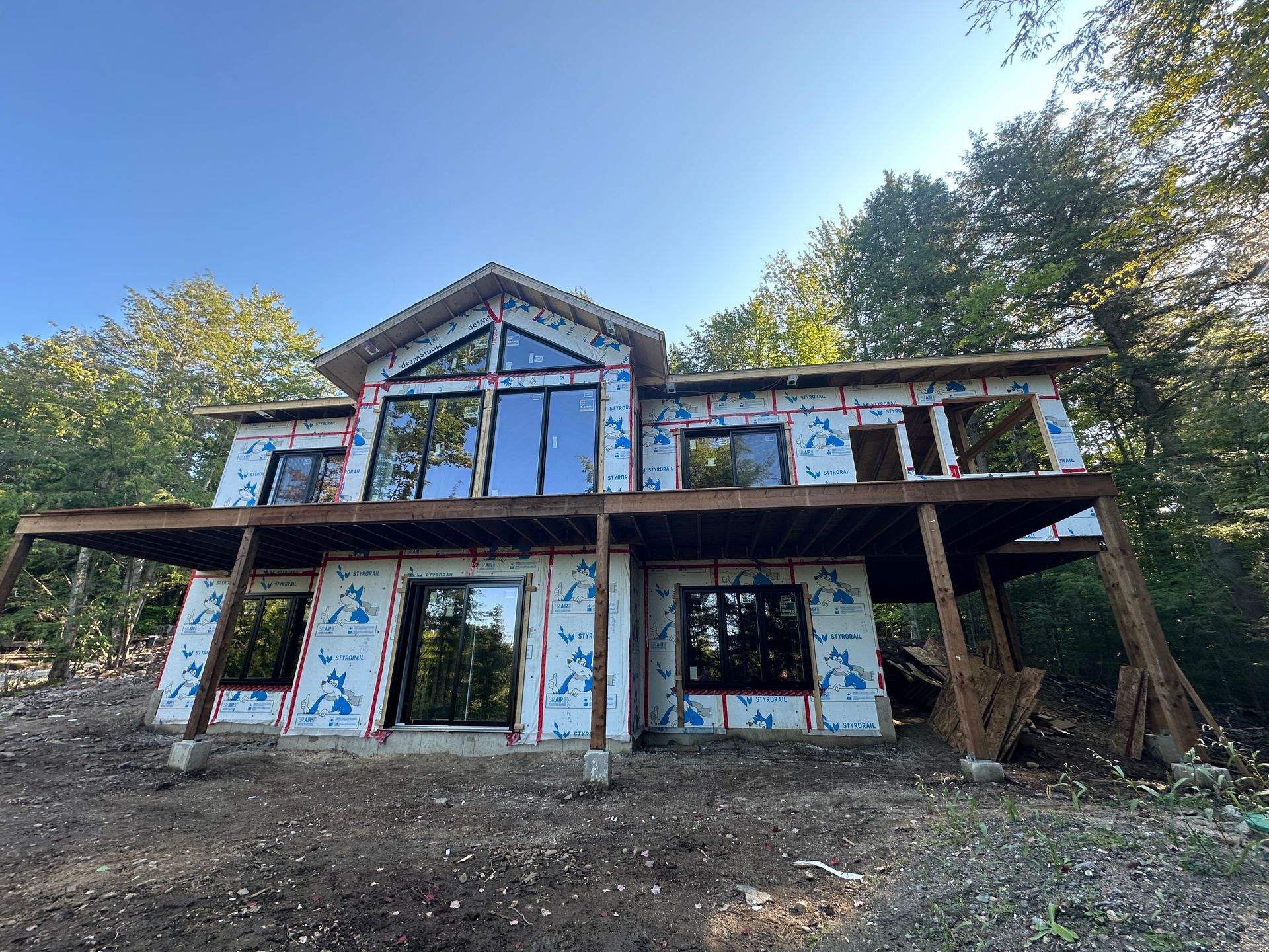 Maison en bois partiellement construite avec de grandes fenêtres sur un flanc de colline boisé