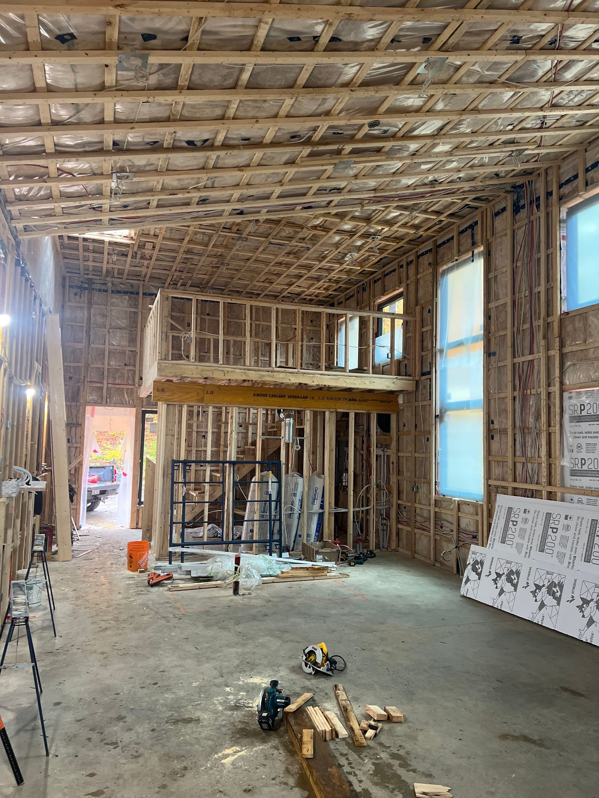Intérieur d'une maison en cours de rénovation, avec charpente apparente, murs nus et débris de construction au sol.