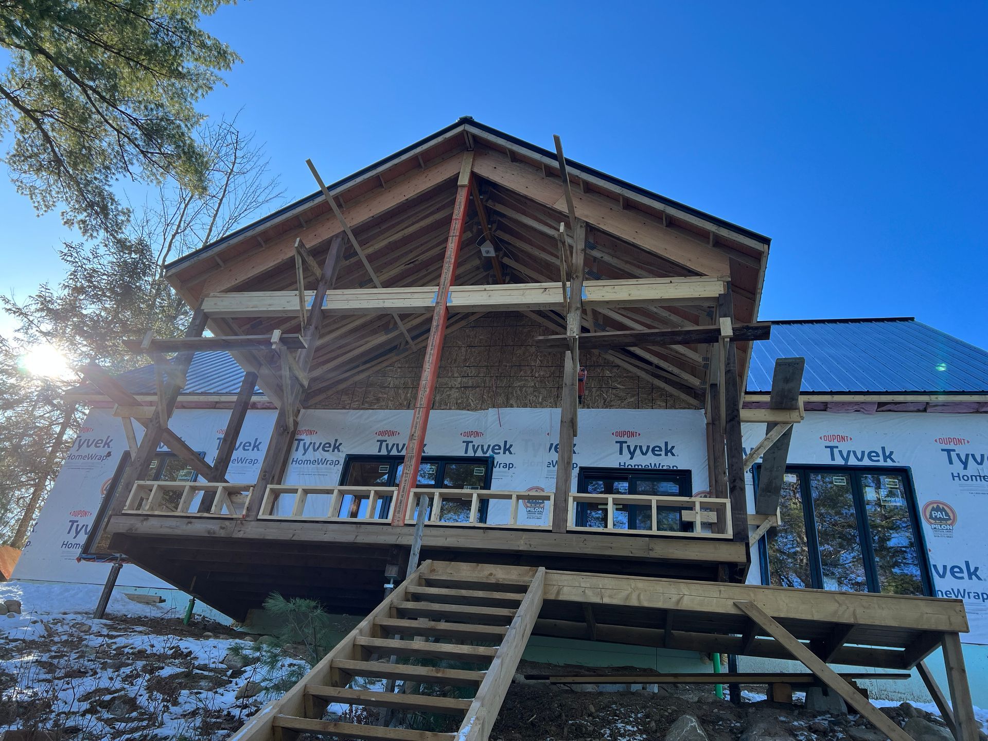 Cabane en bois en construction, avec escalier, charpente apparente et ciel bleu au-dessus