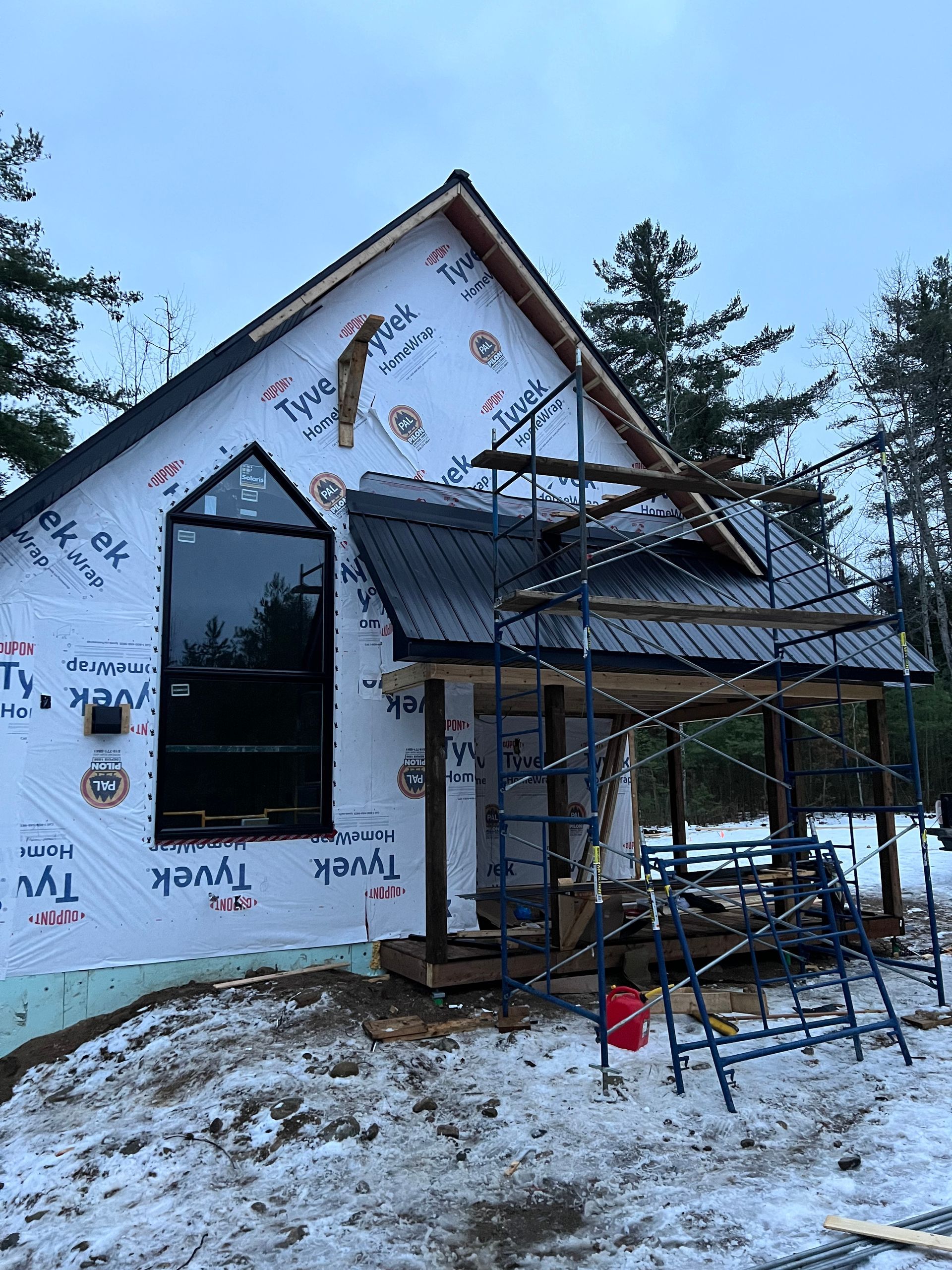 Extérieur de la maison en construction, avec des échafaudages et de la neige au sol.