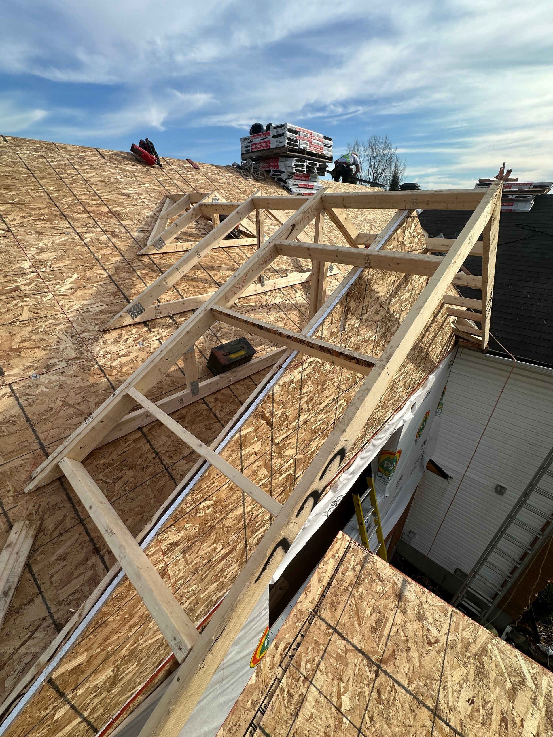 Toiture en construction avec charpente en bois sur un revêtement en contreplaqué à côté d'une maison et d'un paysage enneigé